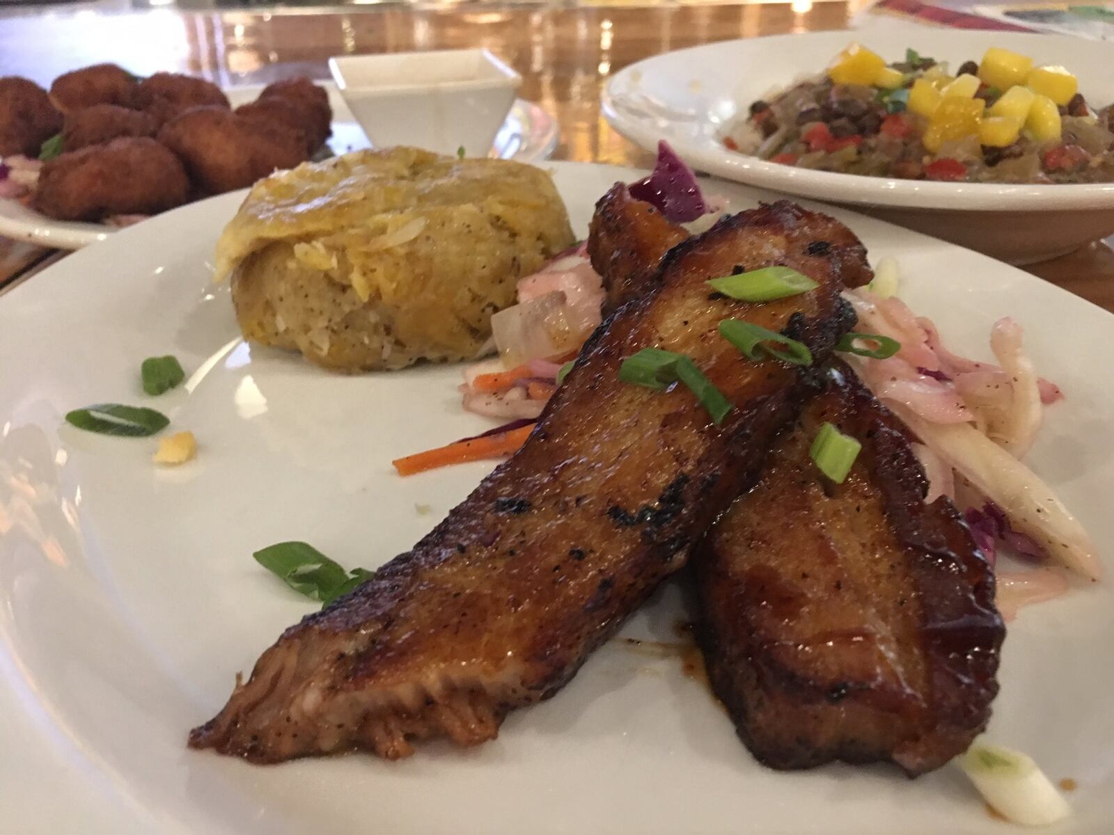 Calypso Pork Belly ($12.99) with Shrimp Pup-a-lickie ($7.49) and pigeon peas and rice ($8.99) in the background. CONTRIBUTED/ALEXIS LARSEN