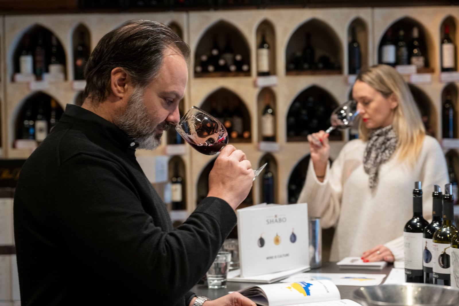 Wine Styles owner Arthur Lampros, left, and Valentyna Parsaieva, head of export for Shabo, a Ukrainian winery, right, take part in a wine tasting at Wine Styles, Dec. 20, 2024 in Dumfries, Va. (AP Photo/Kevin Wolf)