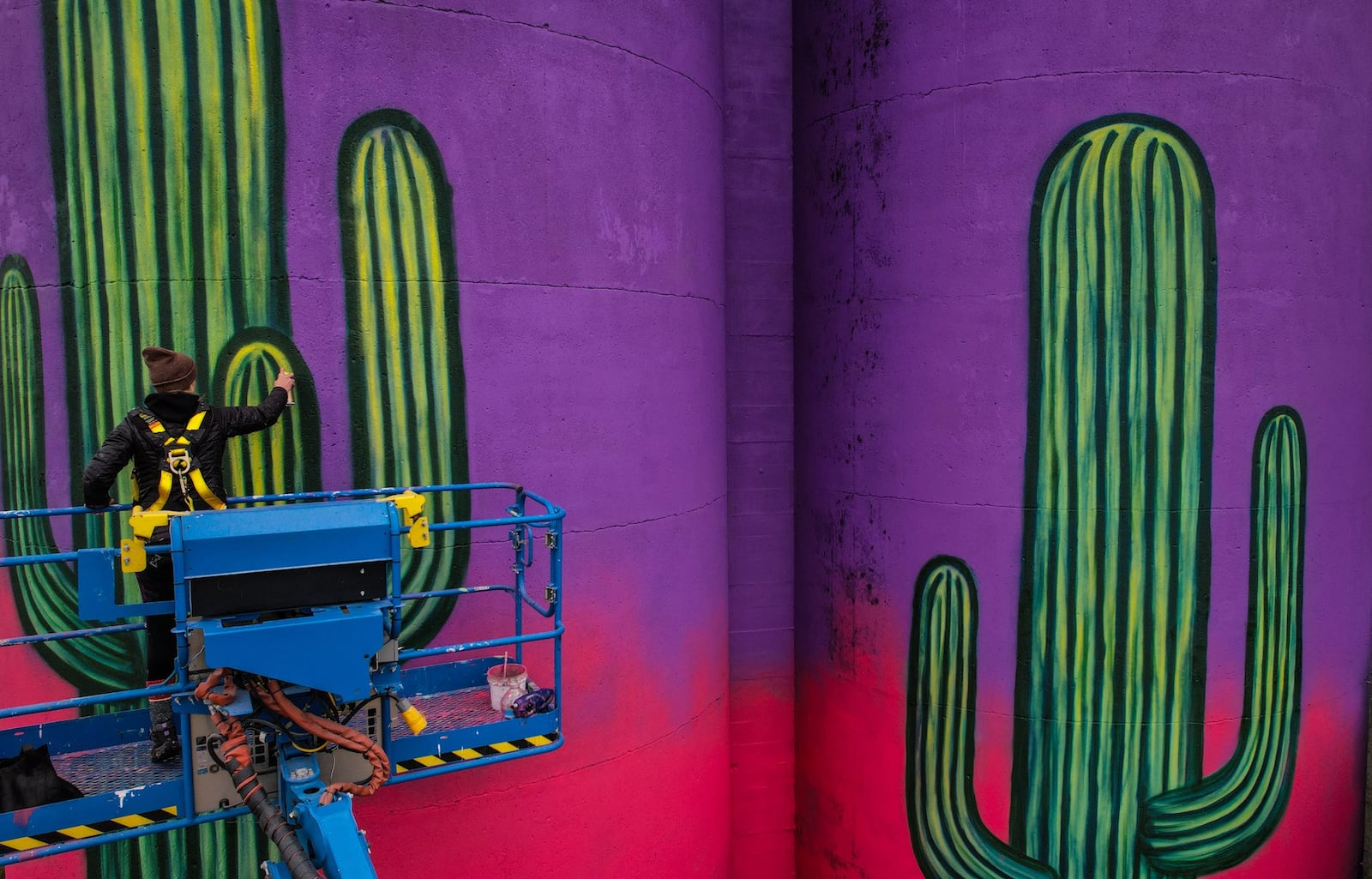 Centerville-raised muralist Erica Arndts paints a desert scene on the silos near 2nd Street Market. JIM NOELKER/STAFF