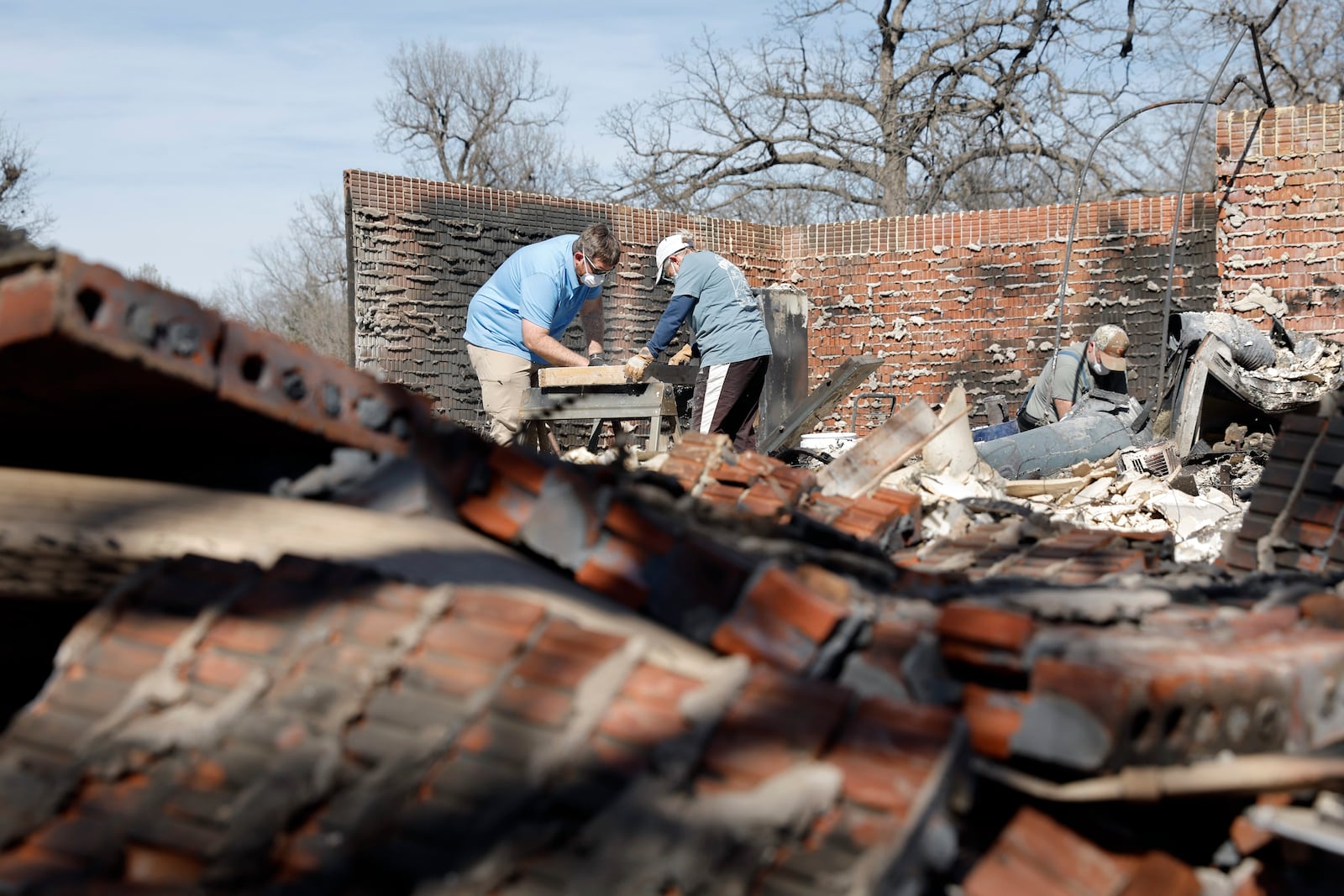 Cayton Jones, left, and his family look through the ashes of his home in the Hidden Oaks neighborhood in Stillwater, Okla., Monday, March 17, 2025, after wildfires burned through the area on Friday. (AP Photo/Alonzo Adams)