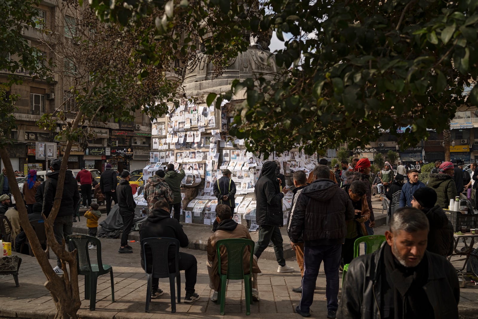 People look at photos of people reported to be missing, by members of ousted Syrian President Bashar Assad's army or a pro-government militia, as others sit to smoke and drink tea at the Marjeh square in Damascus, Syria, Sunday, Dec. 22, 2024. (AP Photo/Leo Correa)