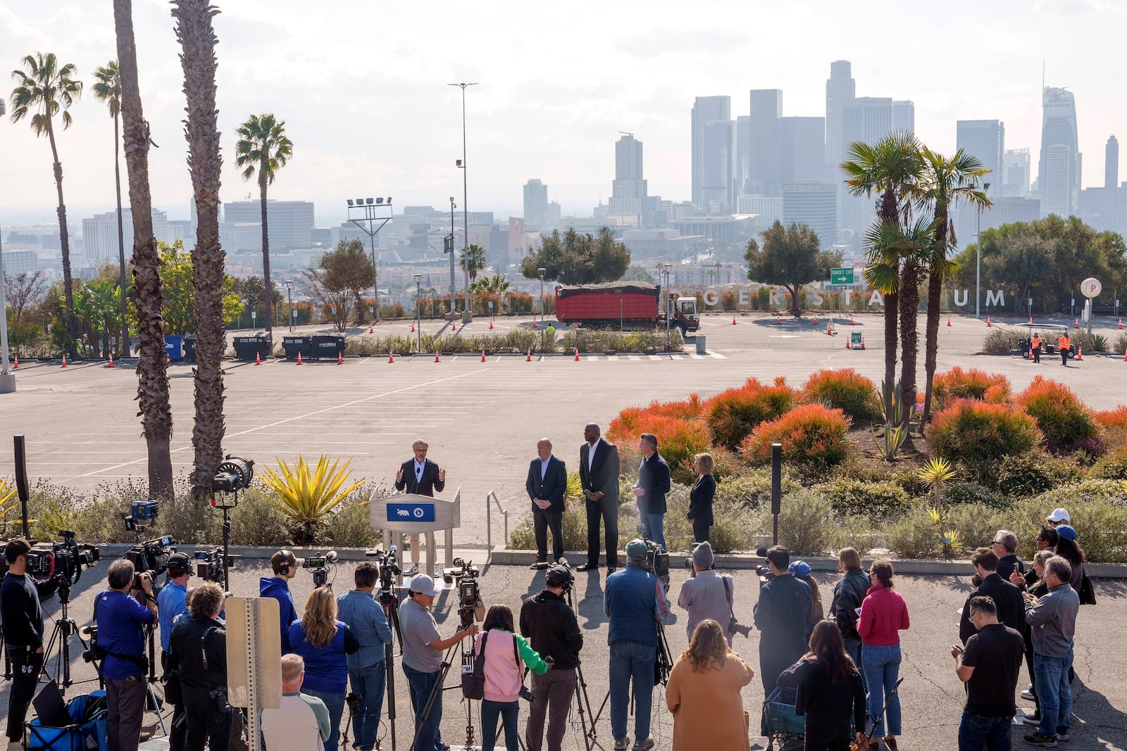 2028 Olympics organizer Casey Wasserman, at podium, introduces Dodgers President and CEO Stan Kasten, from fourth right back, Magic Johnson, and California Gov. Gavin Newsom outside Dodger Stadium overlooking downtown Los Angeles, to announce a new private sector initiative called LA Rises to support rebuilding efforts after the devastating wildfires, Tuesday, Jan. 28, 2025. (AP Photo/Damian Dovarganes)