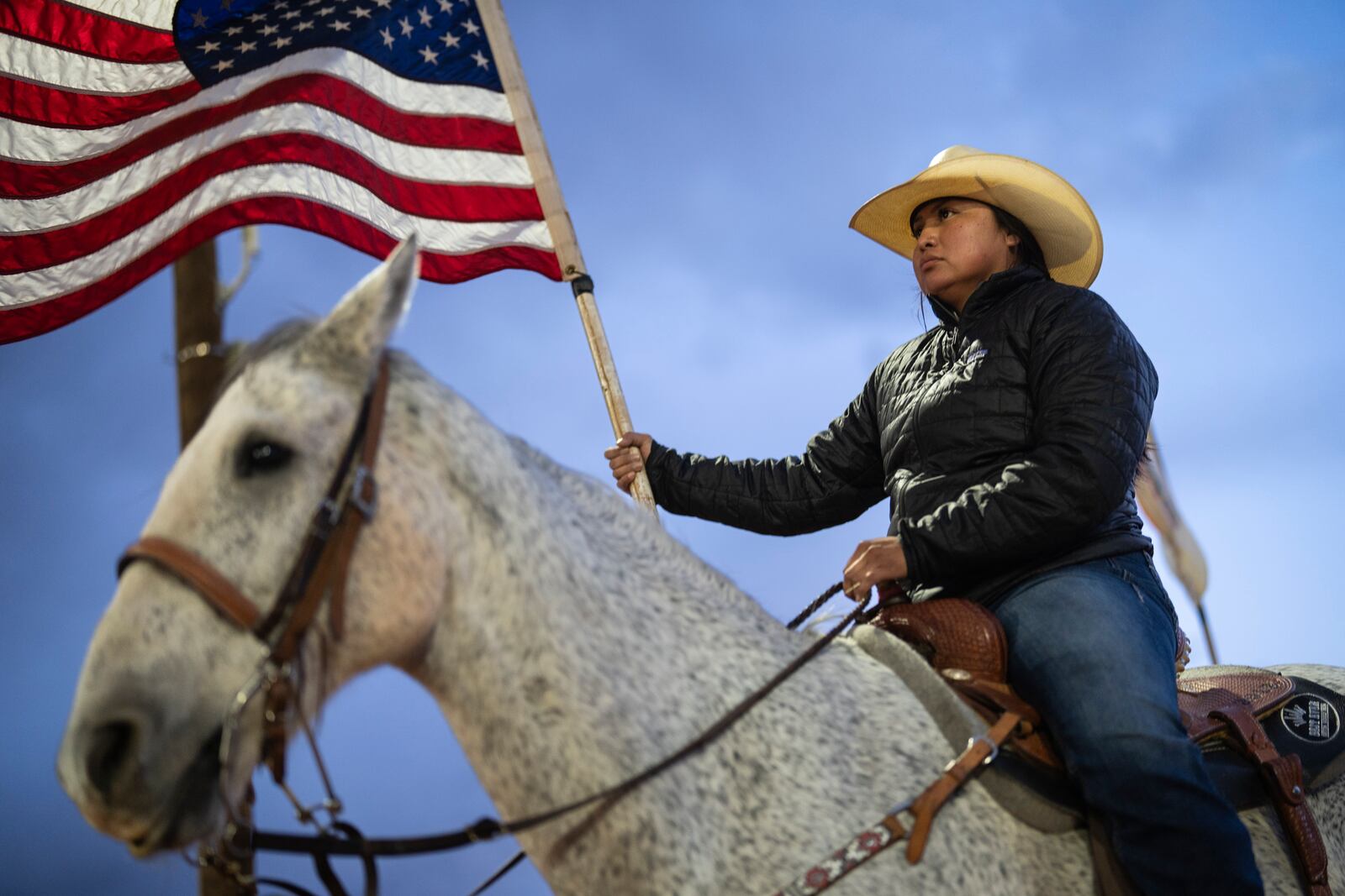 A Navajo horsewoman carries a U.S. flag as she waits for the start of the Western Navajo Fair opening ceremony in Tuba City, Ariz., Friday, Oct. 18, 2024. Native people were first recognized as U.S. citizens 100 years ago, but Arizona prevented them from exercising their right to vote until 1948. (AP Photo/Rodrigo Abd)