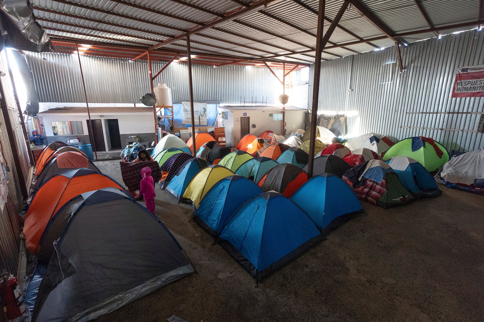 Margelis Rodriguez, of Venezuela, folds a towel alongside her 6-year-old daughter Maickeliys at their tent where the family is staying at a migrant shelter in Tijuana, Mexico, Saturday, Feb. 1, 2025. (AP Photo/Gregory Bull)