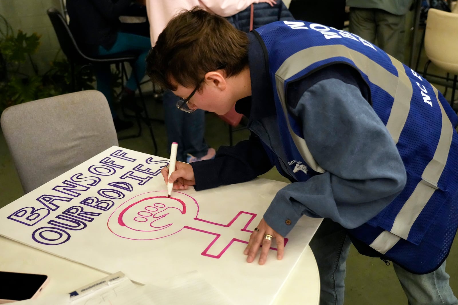 Cole Archer works on a protest sign during a meeting of NC Forward in High Point, N.C., Tuesday, Jan. 14, 2025. The group is traveling to Washington to take part in the People's March on Jan. 18 ahead of the inauguration. (AP Photo/Chuck Burton)