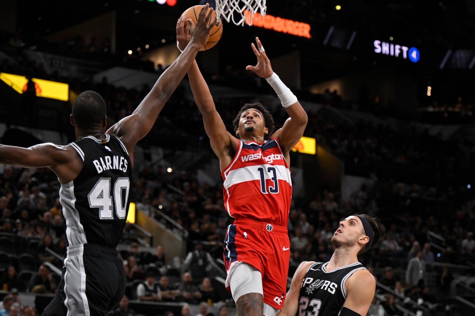 Washington Wizards' Jordan Poole (13) goes to the basket against San Antonio Spurs' Harrison Barnes (40) and Zach Collins during the first half of an NBA basketball game, Thursday, Nov. 13, 2024, in San Antonio. (AP Photo/Darren Abate)