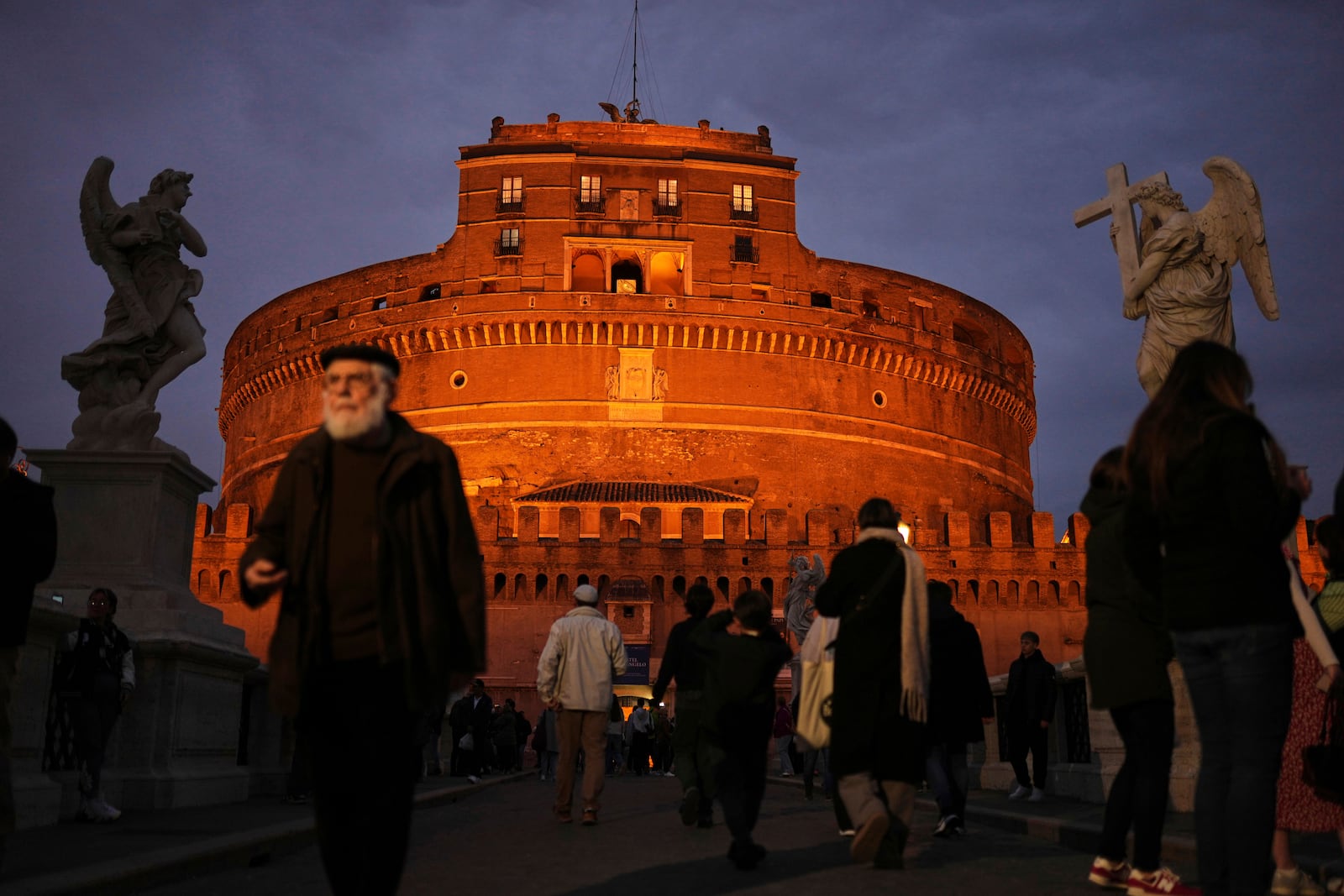 Locals and tourists walk outside the Sant'Angelo castle as the sun sets in Rome, Italy, Friday, March 7, 2025. (AP Photo/Francisco Seco)