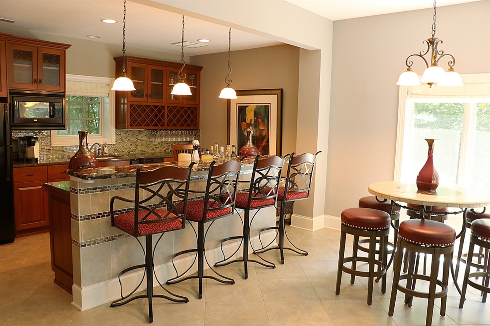 The lower-level kitchen has mahogany cabinetry with bubble-glass panel doors that surround appliances, including a refrigerator, microwave and dishwasher. A window is above the double sink, and cabinetry includes bottle and glass racks. CONTRIBUTED PHOTO BY KATHY TYLER