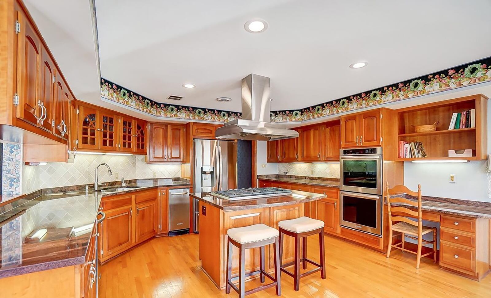 The updated kitchen has an island with bar seating, stainless range hood, gas cooktop and updated stainless appliances.