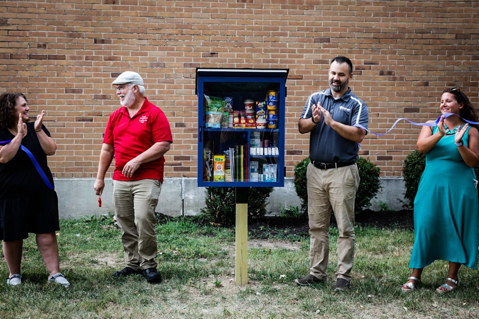 From left, Valerie Dupler, from Kettering schools, Don Bennett, from Good Shepard Lutheran Church, Daniel Koons, from DayAir and Jesska Stickel, from Kettering City Schools Forward Foundation cut the ribbon on a new community cupboard on Ackerman Blvd. Wednesday September 6, 2023. The mini food pantry is there to help with food insecurity in schools and suburbs. JIM NOELKER/STAFF