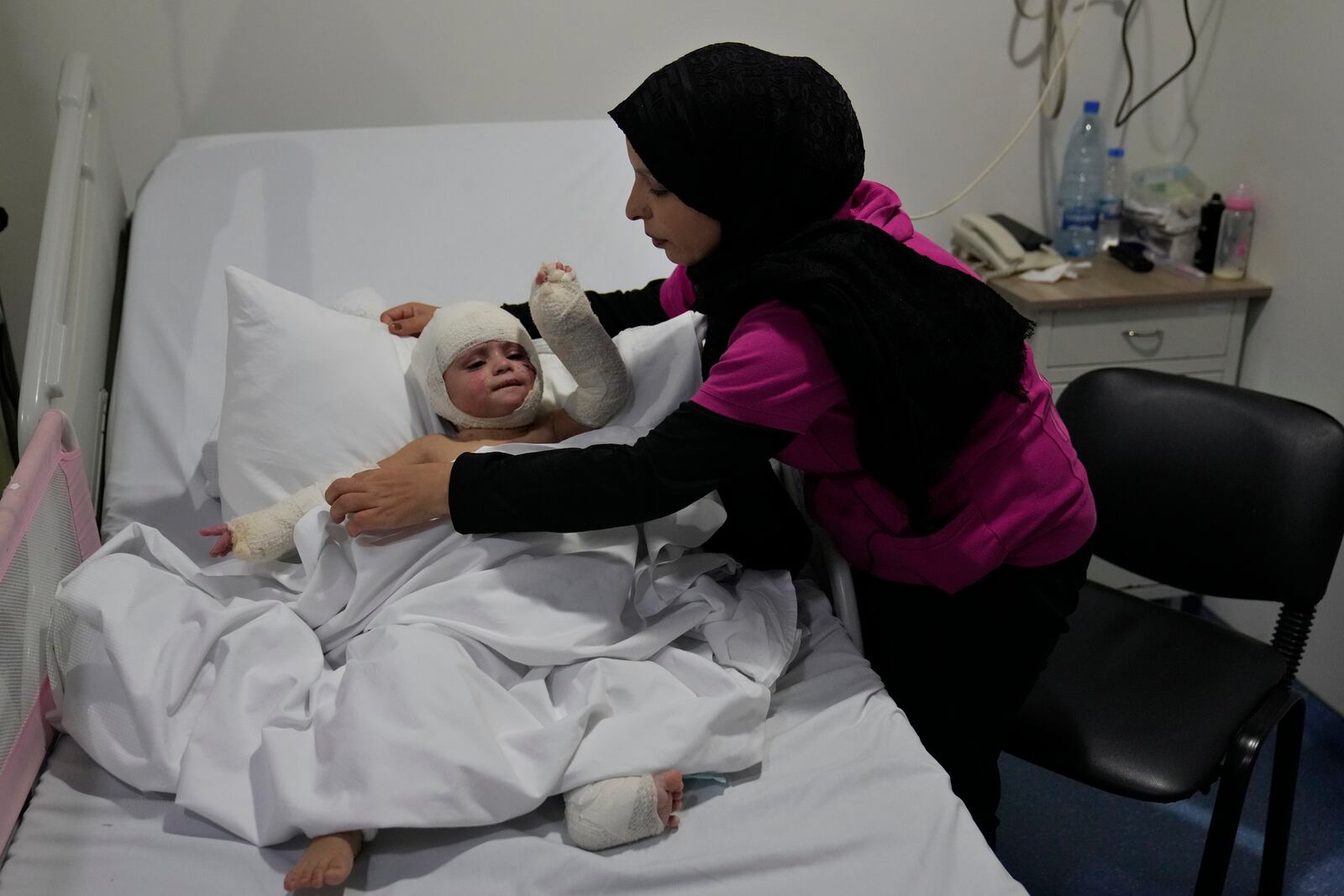 Fatima Zayoun, covers her daughter Ivana Skakye, 2, who is suffered for third-degree burns over 40 percent of her body following an Israeli airstrike last September near their home in Deir Qanoun al Nahr a village in south Lebanon, as she lies on the bed at the Lebanese hospital Geitaoui where she is receiving treatment, in Beirut, Lebanon, Tuesday, Oct. 29, 2024. (AP Photo/Hussein Malla)