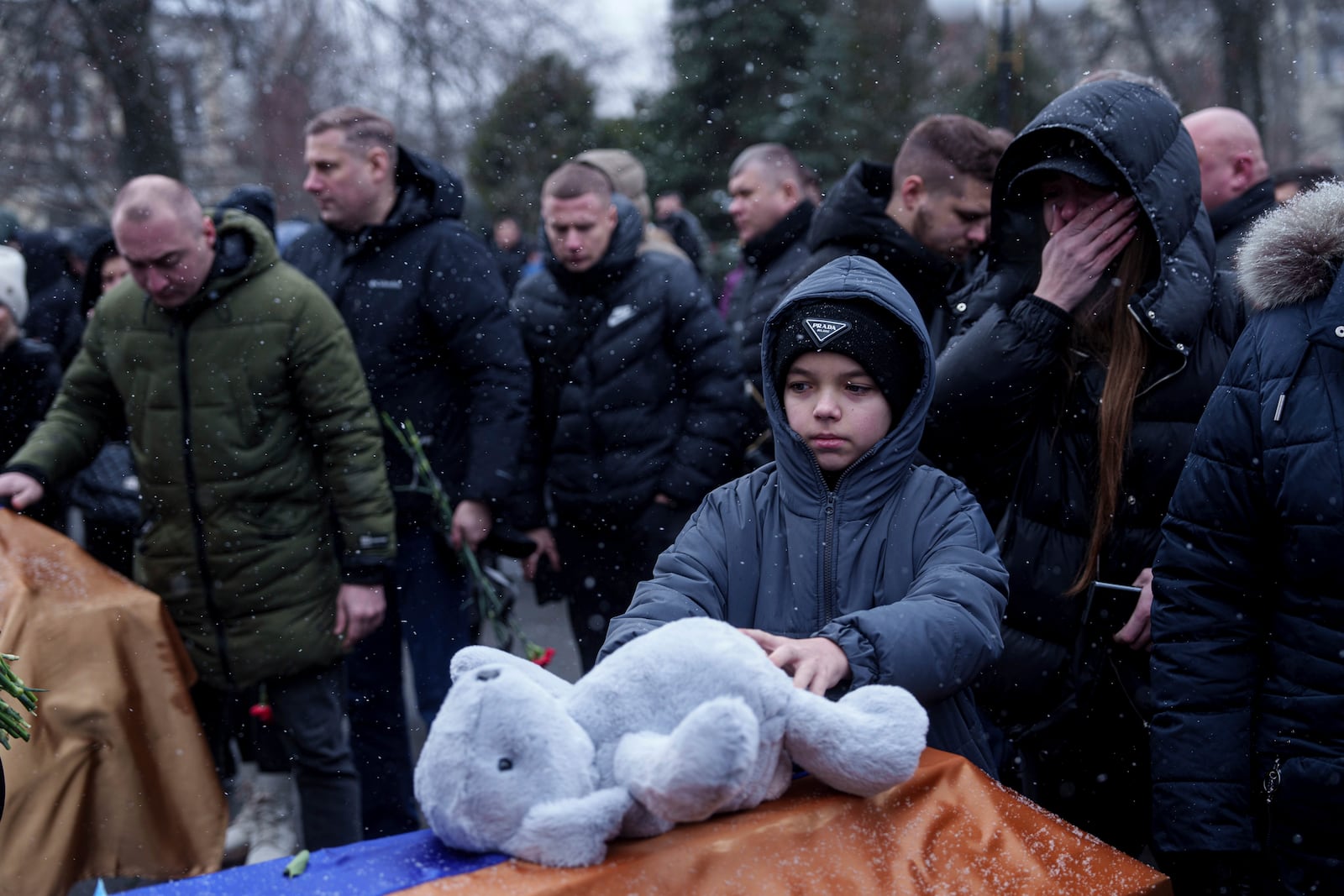 A boy puts a toy on a coffin as he says goodbye to Dmytro Yavorskyi, 37, Sofia Yavorska, 9, Olena Yavorska 38, who were killed on Feb. 1 by a Russian strike on residential building during a funeral ceremony in Poltava, Ukraine, Wednesday, Feb. 5, 2025. (AP Photo/Evgeniy Maloletka)