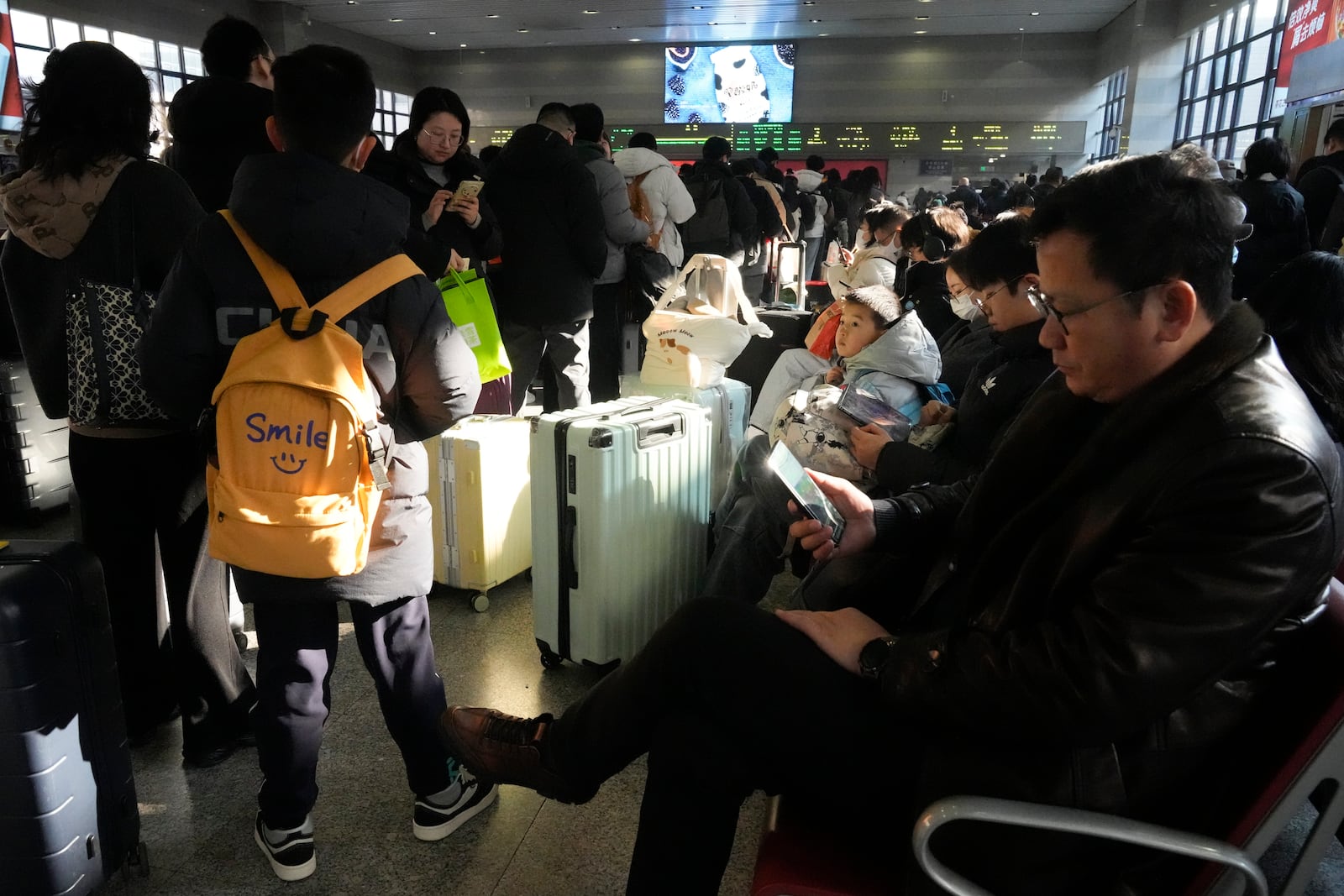 Travelers sit at the waiting area at the departure hall to catch their trains at the Beijing West Railway Station ahead of the Lunar New Year in Beijing on Friday, Jan. 24, 2025. (AP Photo/Aaron Favila)