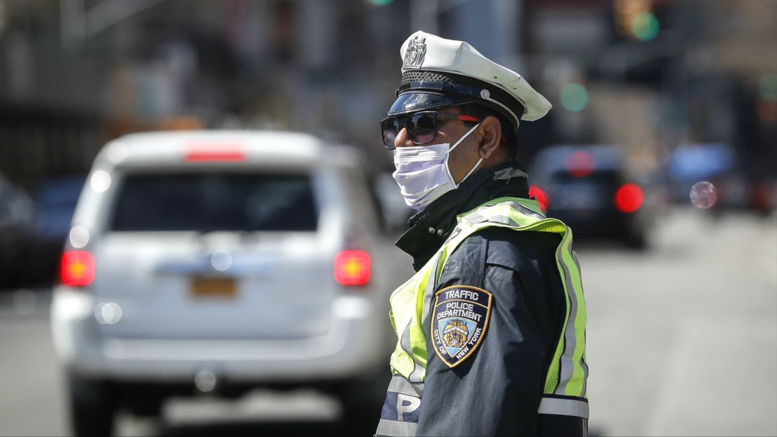 A New York police officer wearing personal protective equipment stands March 27, 2020, near a barricade shutting down part of Bushwick Avenue due to COVID-19. NYPD officials announced Wednesday, April 15 that the department had lost its 26th and 27th employees to the coronavirus pandemic. (AP Photo/John Minchillo)