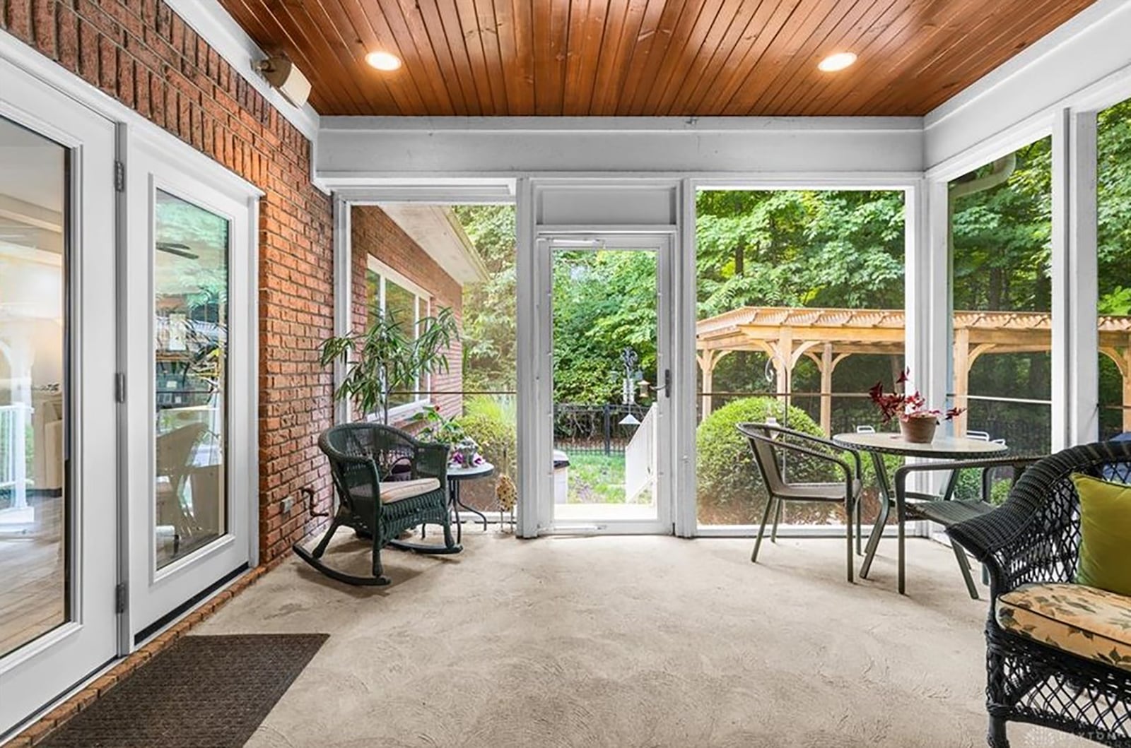 The sun room is screened on all sides, has a stamped concrete patio, beadboard ceiling, and it opens to the concrete walkway leading to the patio with wood pergola.