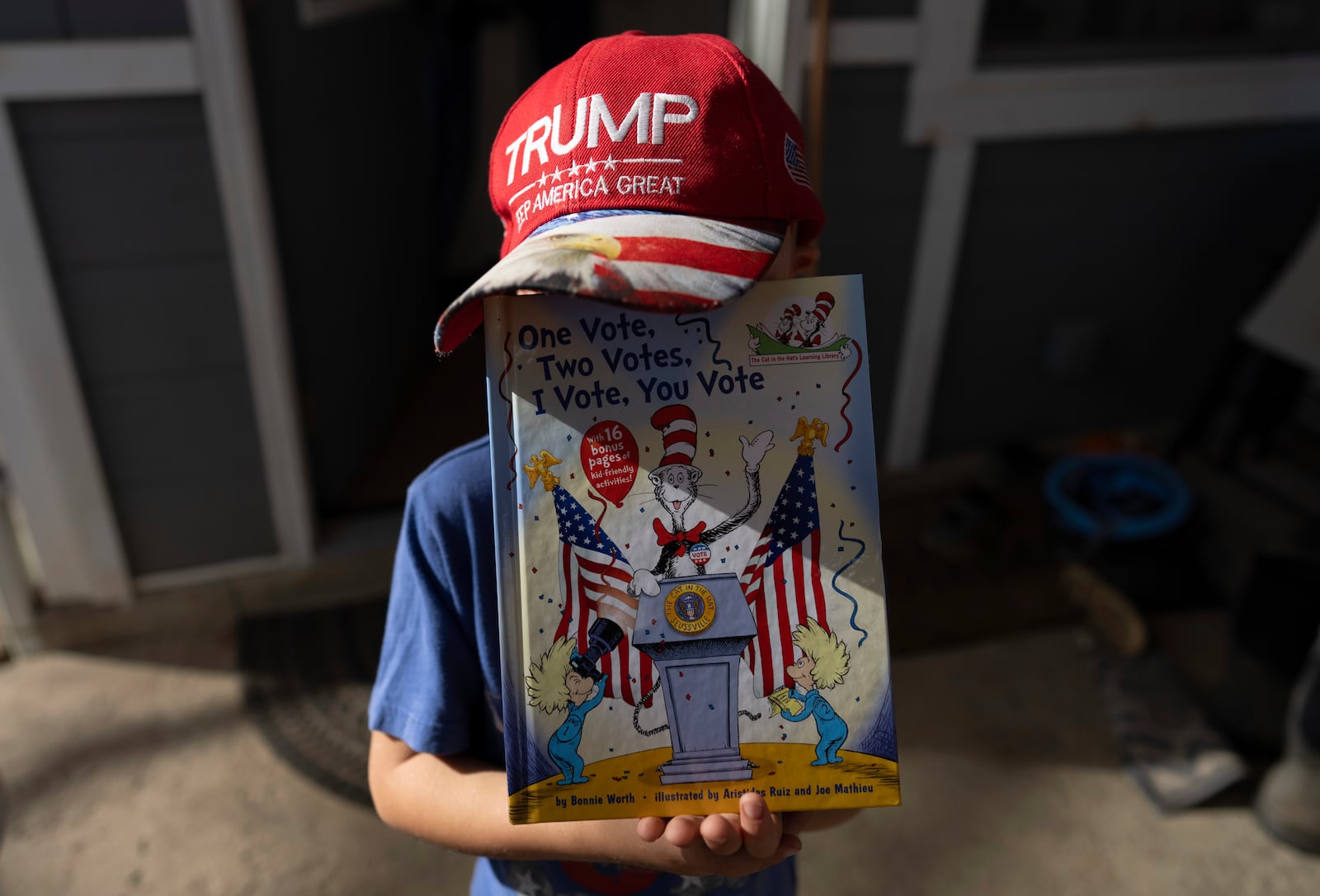 Isaac Young, 5, wears his "TRUMP Keep America Great" hat as he holds up the book, "One Vote, Two Votes, I Vote, You Vote of The Cat in the Hat's Learning Library" by Bonnie Worth, illustrated by Aristides Ruiz, and Joe Mathieu, before going to watch his dad, Mike Young, vote for Donald Trump on Election Day, Tuesday, Nov. 5, 2024, in Sunbury, Ohio. (AP Photo/Carolyn Kaster)