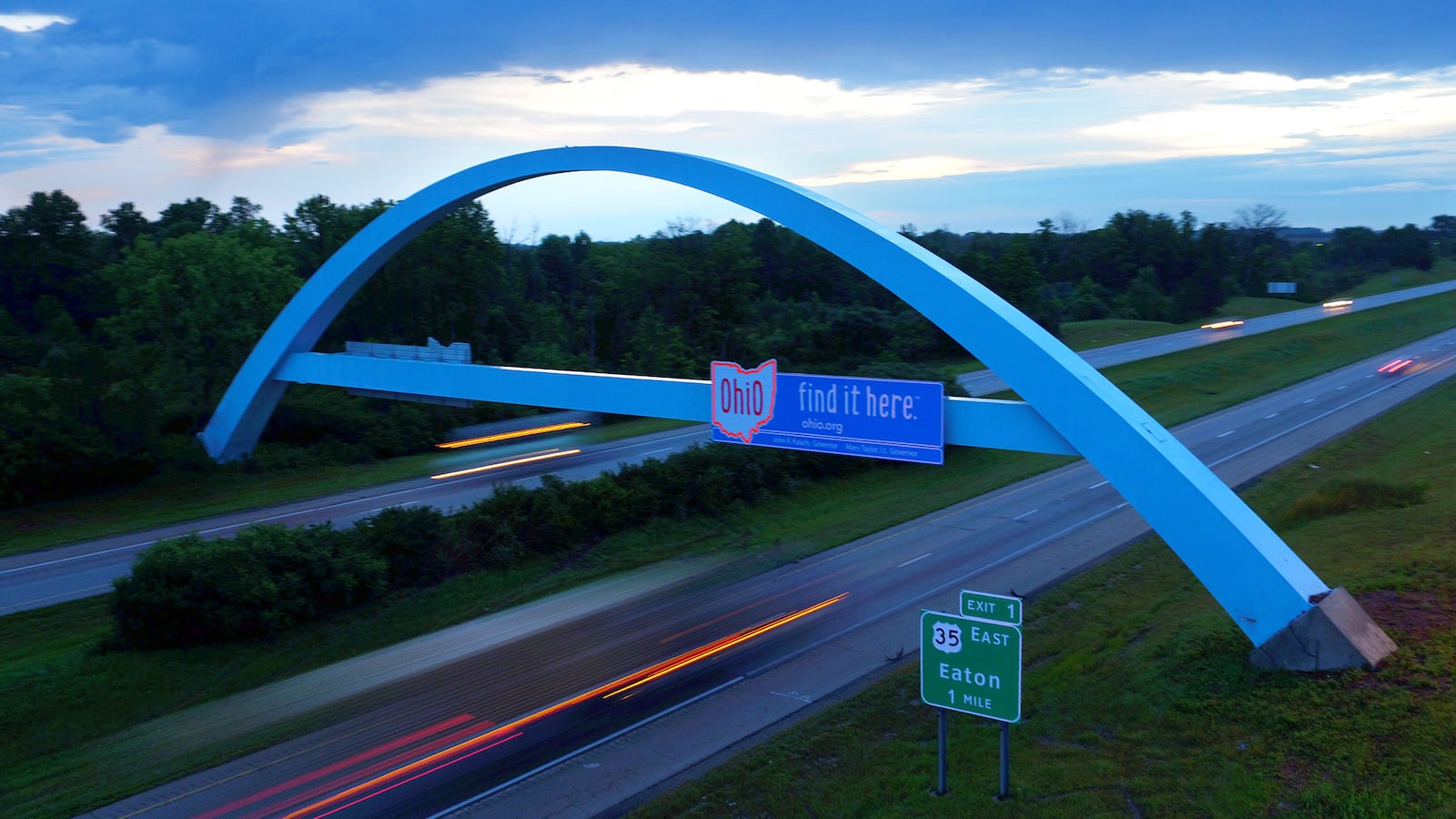 The arch welcoming motorists into Ohio is blue in the pre-dawn twilight on I-70 in Preble County.  The lights on cars and trucks are blurred from a slow shutter speed.  JAROD THRUSH / STAFF