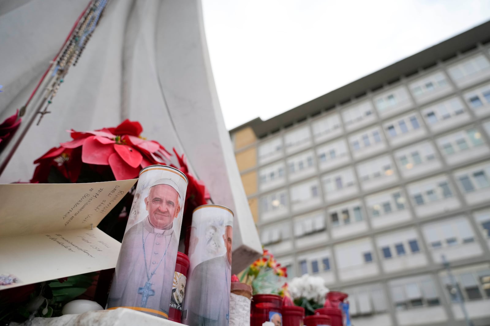 Candles with the pictures of Pope Francis are the laid under the statue of late Pope John Paul II outside Agostino Gemelli Polyclinic in Rome, Wednesday, Feb. 19, 2025, where the Pontiff is hospitalized since Friday, Feb. 14. (AP Photo/Gregorio Borgia)