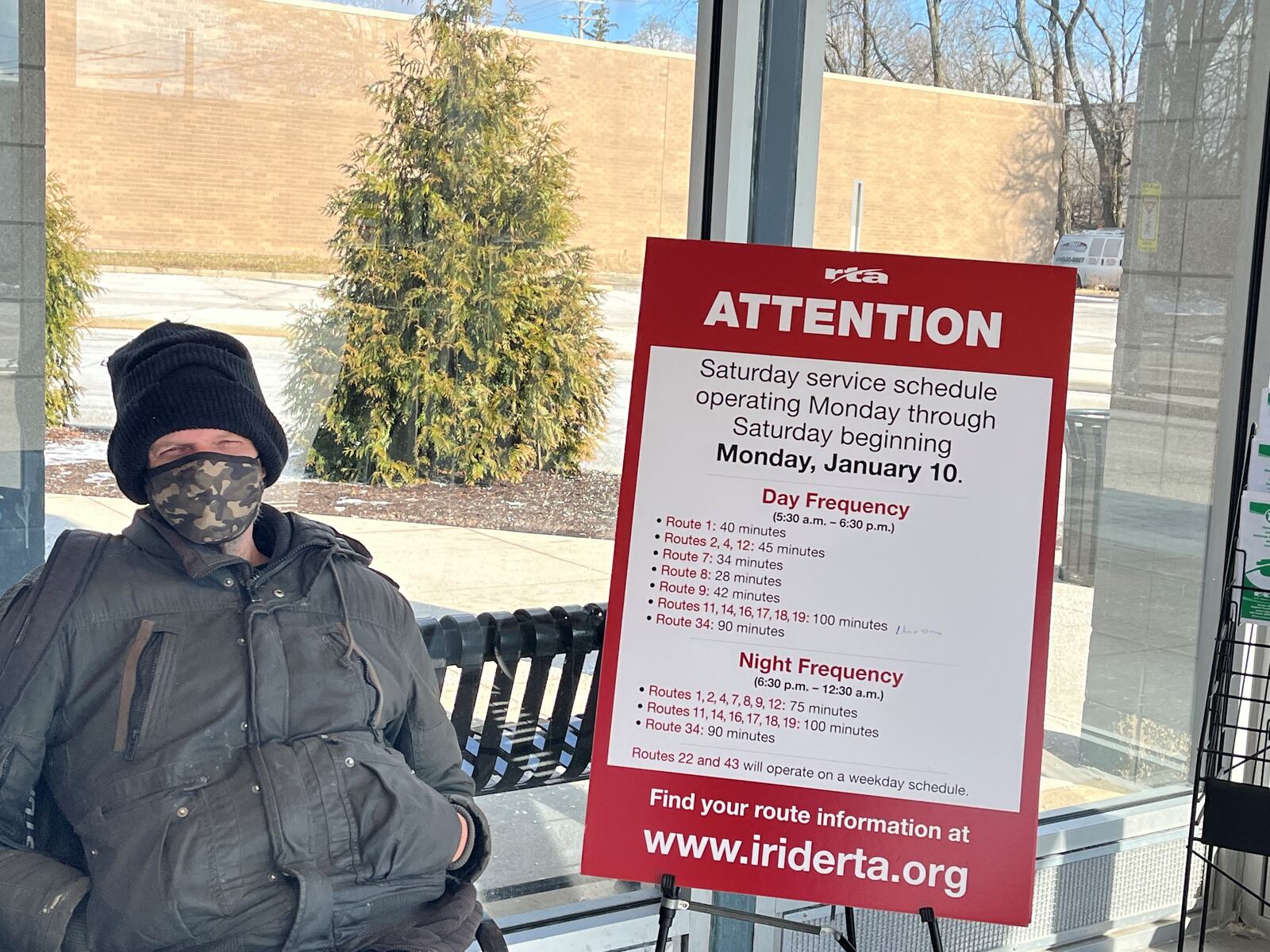 A man sits at the Greater Dayton RTA Eastown Transit Center, next to a sign about service changes. CORNELIUS FROLIK / STAFF