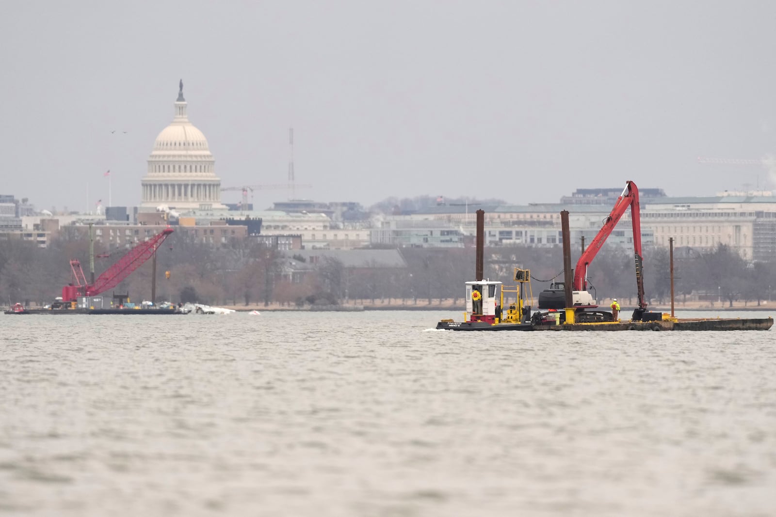 With the U.S. Capitol in the background, cranes are pictured in the Potomac river Sunday, Feb. 2, 2025, near the wreckage of an American Airlines jet, at left, that collided mid-air with an Army Black Hawk helicopter in Arlington, Va., as seen from Alexandria, Va. (AP Photo/Carolyn Kaster)