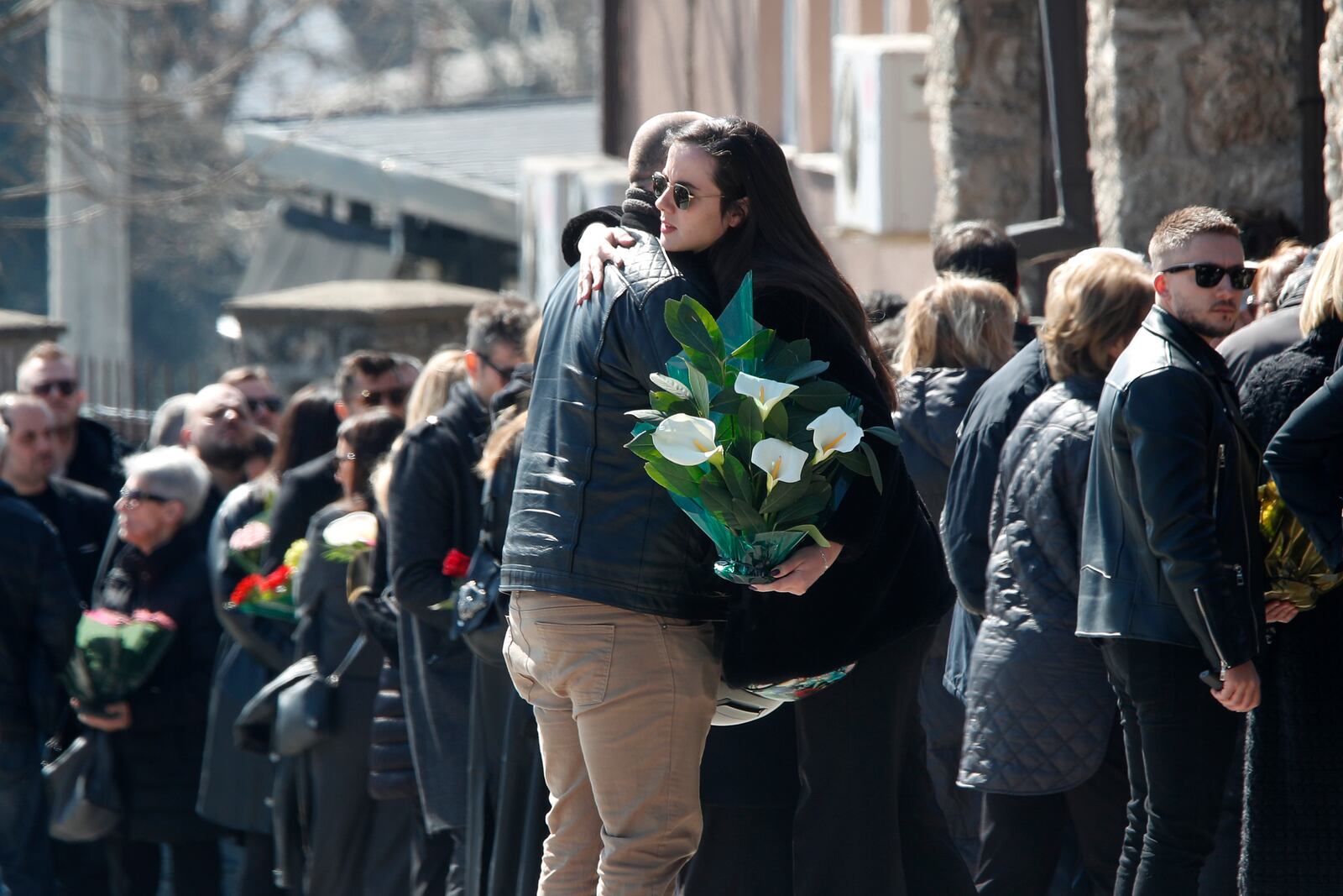 People hug as they arrive for the funeral of Andrej Gjorgieski, one of the lead singers of Macedonian band DNK, a victim of the March 16 nightclub fire in the town of Kocani, at a cemetery in Skopje, North Macedonia, Thursday, March 20, 2025. (AP Photo/Boris Grdanoski)