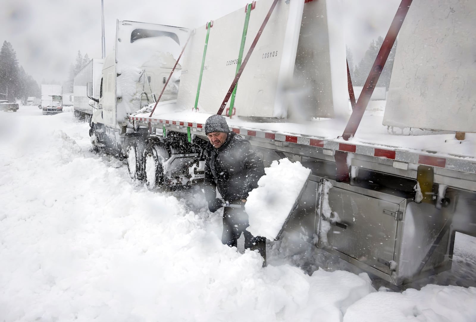 Truck driver Kirill Foken shovels a trench alongside his truck's tires to free it up as he awaits for I-5 to reopen in Weed, Calif., Wednesday, Nov. 20, 2024. (Carlos Avila Gonzalez/San Francisco Chronicle via AP)