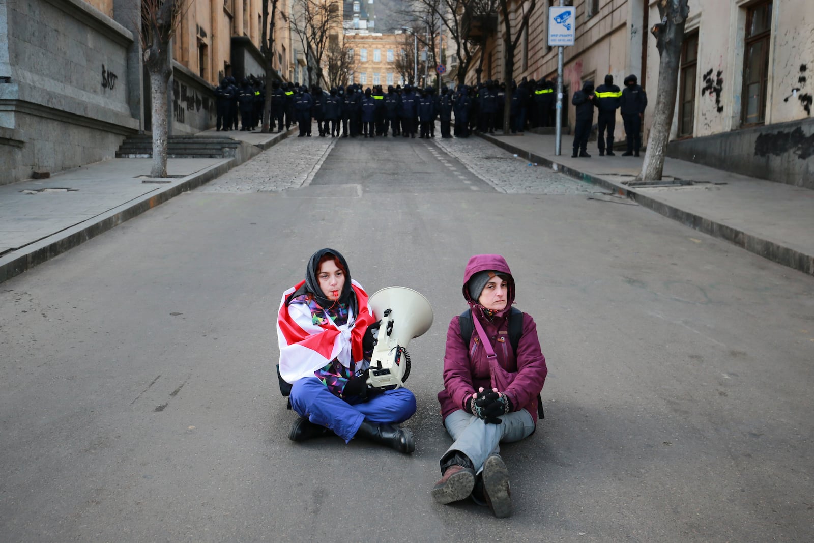 Protesters sit on a street as police block the street outside the Georgian parliament while the parliament has begun the procedure of the presidential elections, in Tbilisi, Georgia, Saturday, Dec. 14, 2024. (AP Photo/Zurab Tsertsvadze)