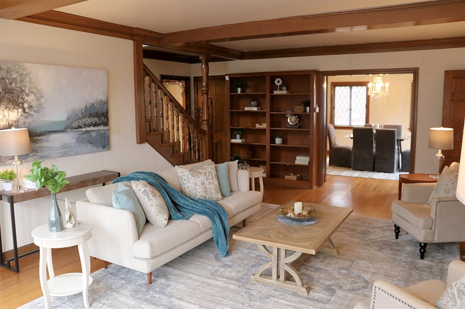 The living room has refinished hardwood flooring and large leaded-glass windows. Wood beams cross the ceiling and connect with the crown molding.