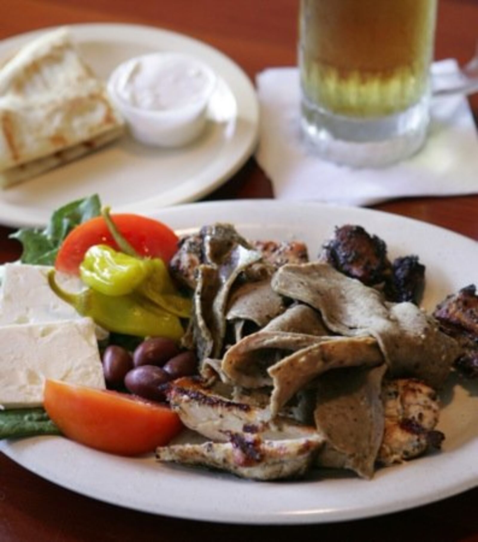 A Greek Hot Plate (for one), is a gyro made from beef/lamb, chicken breast and pork. Pita bread, with tzatziki sauce (background) is served with the meal. This sells for $9.50 at Tickets Pub and Eatery.