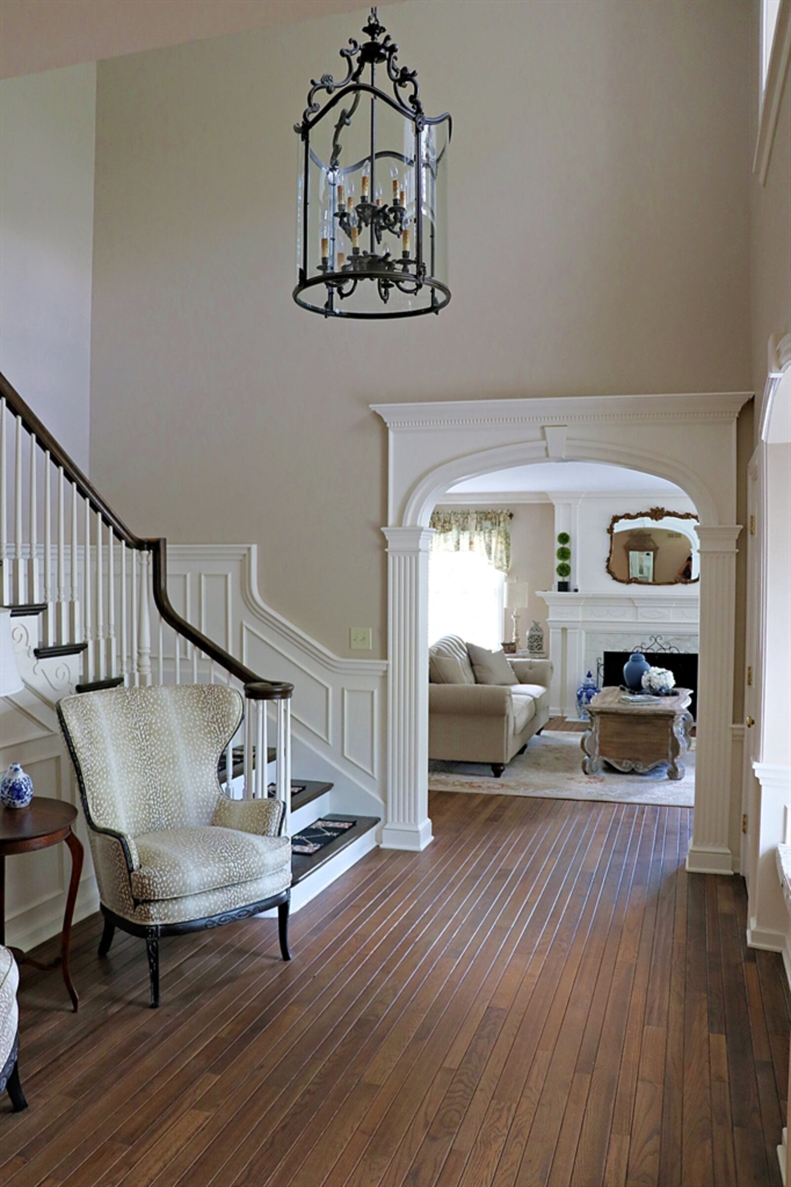 The double-door formal entry opens into the two-story foyer with refinished hardwood flooring. The open staircase has an ornate design with wood steps and banister railing.