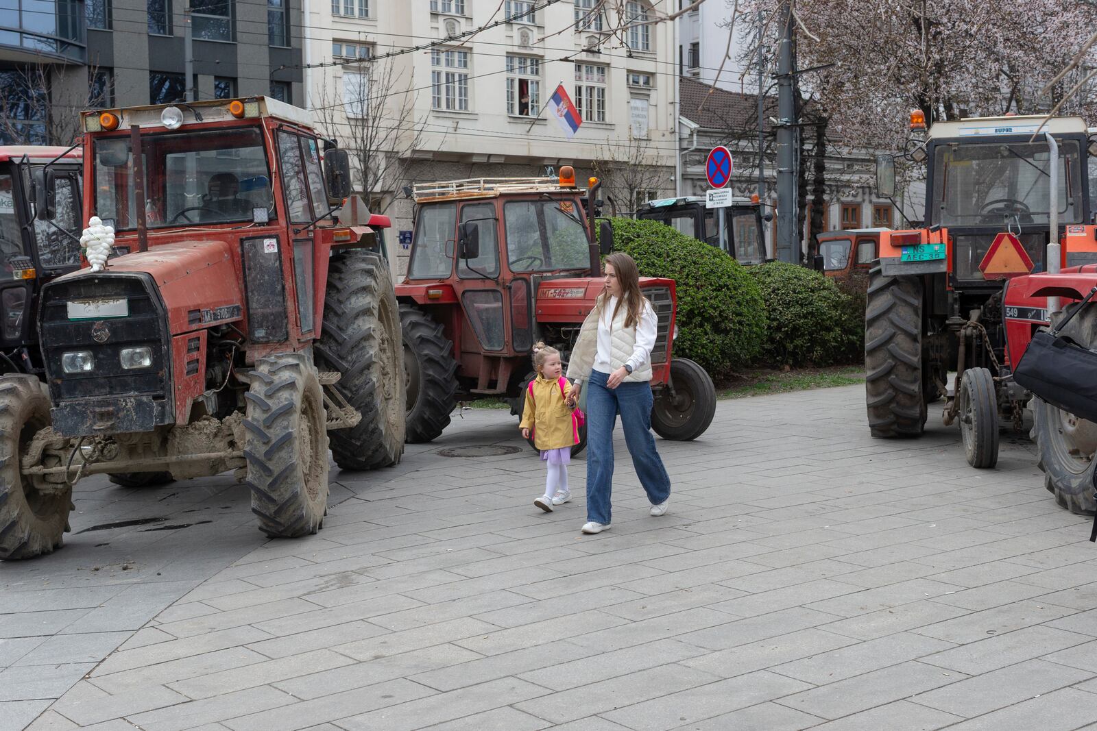 A woman and a child walk past tractors brought in by supporters of the Serbian president Aleksandar Vucic parked on a walkway in Belgrade, Serbia, Friday, March 14, 2025, as the country prepares for a major anti-corruption rally this weekend. (AP Photo/Marko Drobnjakovic)