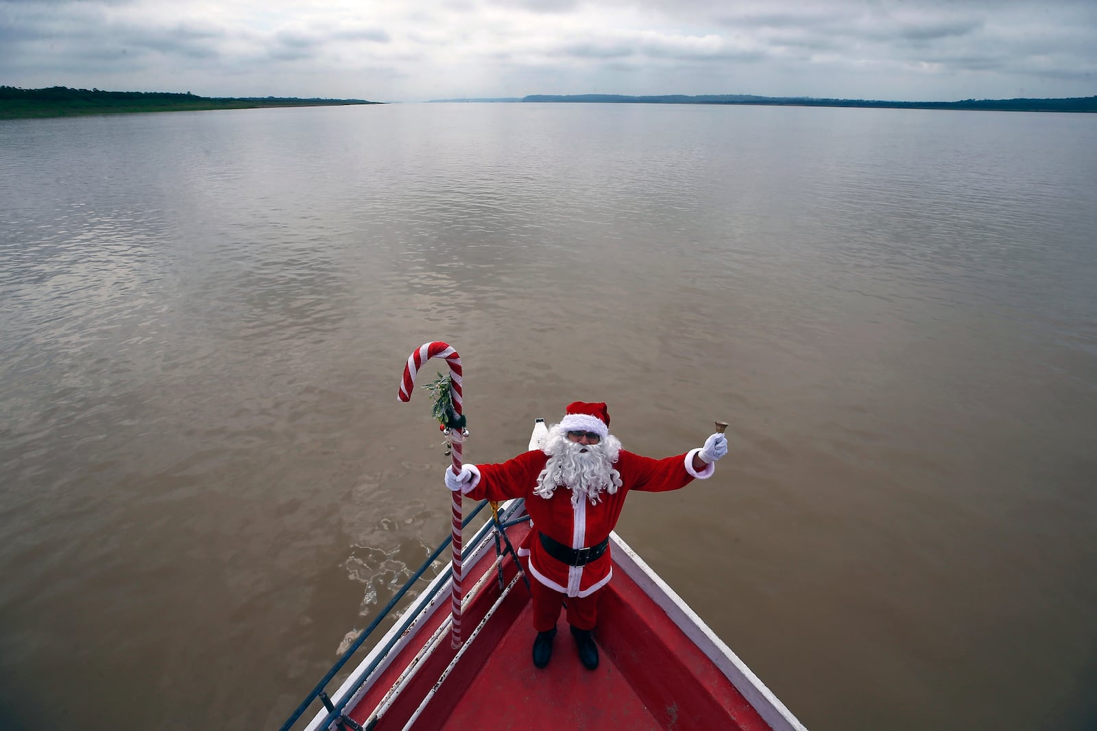 FILE - Jorge Barroso, dressed as Santa Claus, stands on his boat while sailing to visit a community along the jungle shoreline to give out presents to children in the Amazon basin, near Careiro da Varzea, Amazonas state, Brazil, Saturday, Dec. 16, 2023. (AP Photo/Edmar Barros, File)