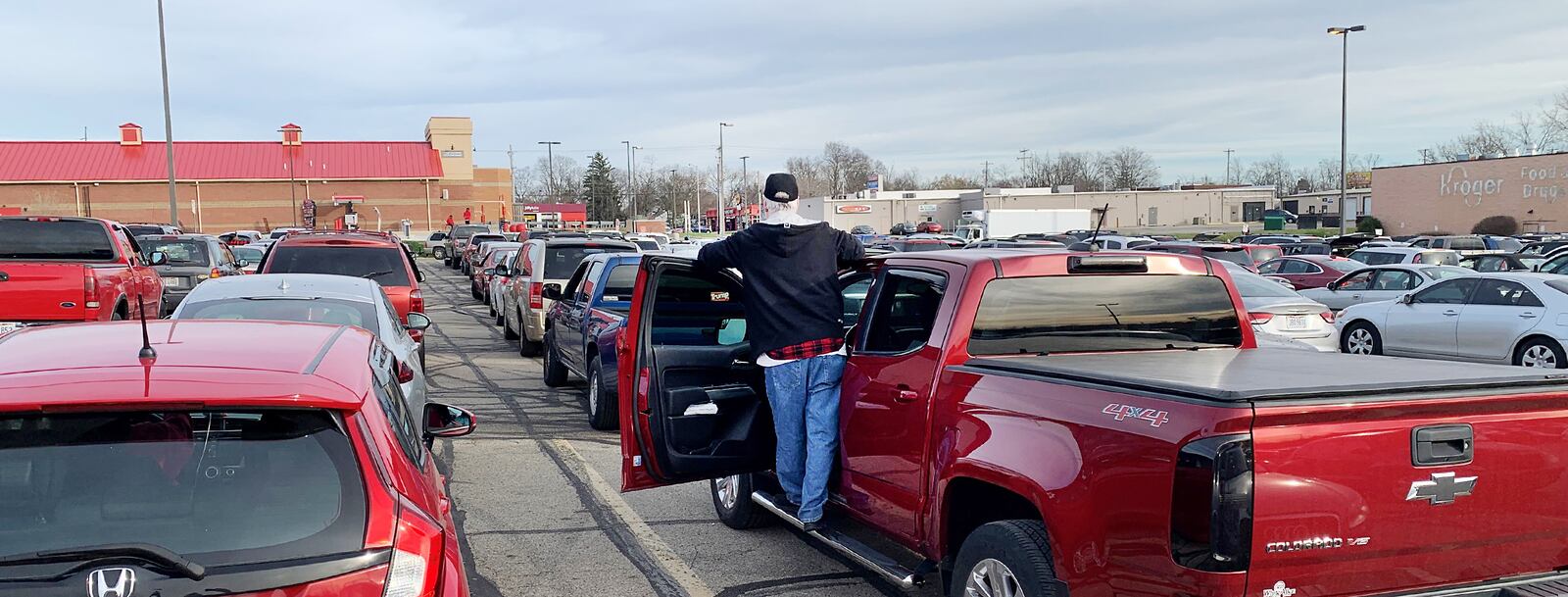 Bob Hess, an Army veteran from Dayton who served in Vietnam, stood on a running board of his pickup last week trying to gauge his wait for a free turkey in a packed parking lot of a vacated Kroger store in Harrison Twp. CHRIS STEWART/STAFF