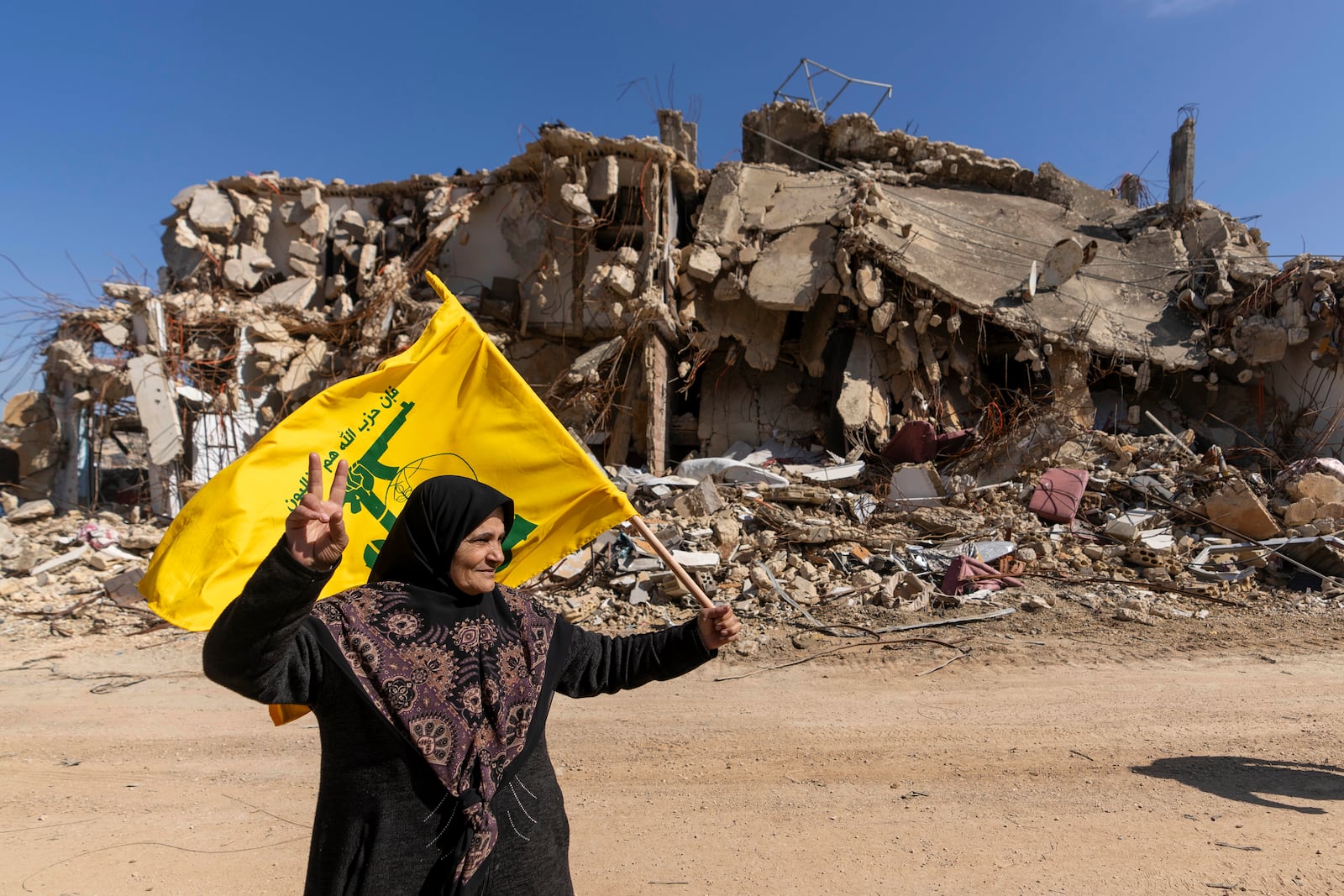 A Lebanese woman holds Hezbollah flag in her village destroyed by the Israeli air and ground offensive, in the town of Kfar Kila, southern Lebanon, Tuesday, Feb. 18, 2025. (AP Photo/Hassan Ammar)