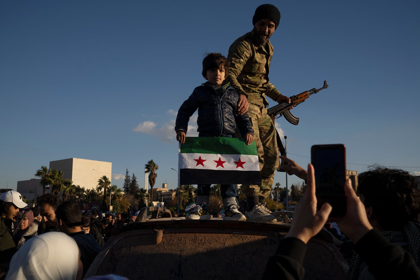 A boy holds a "revolutionary" Syrian flag as he poses for a picture with a Syrian fighter during a celebratory demonstration following the first Friday prayers since Bashar Assad's ouster, in Damascus' central square, Syria, Friday, Dec. 13, 2024. (AP Photo/Leo Correa)