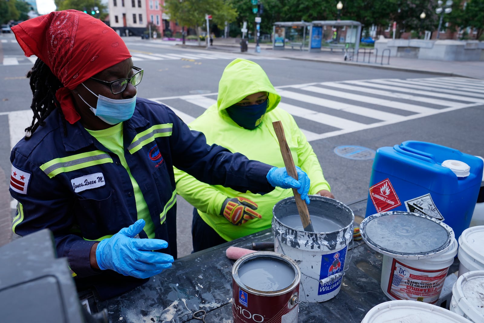 Queen Jones, left, stirs paint as Dominique Medley, right, watches, Tuesday, Aug. 20, 2024, as they prepare to remove graffiti in a neighborhood of Washington. (AP Photo/Susan Walsh)