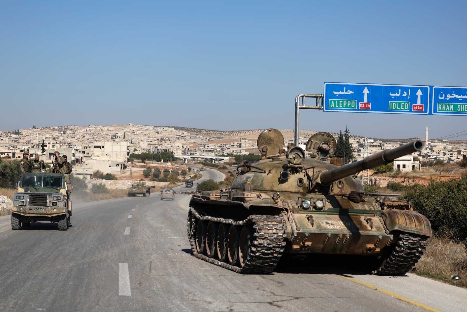 Syrian opposition fighters drive by an abandoned Syrian army armoured vehicle on a highway in the outskirts of in Khan Sheikhoun, southwest of Aleppo, Sunday, Dec. 1, 2024. Syrian opposition insurgency launched a campaign on Wednesday with a two-pronged attack on Aleppo and the countryside around Idlib.(AP Photo/Ghaith Alsayed)