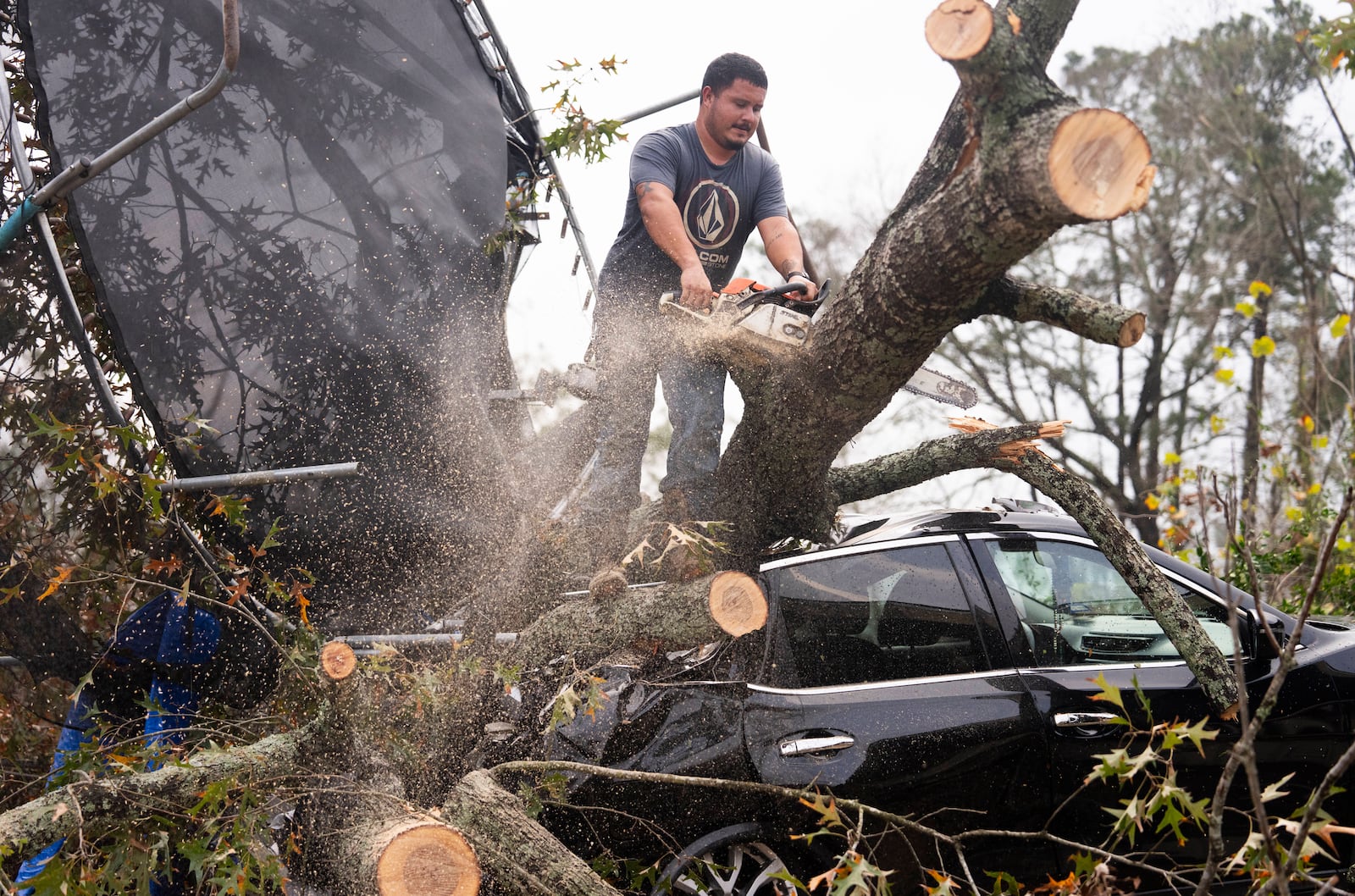 Saul Rodriguez uses a chain saw to remove debris atop a car from a woman's home after strong thunderstorms pass through the Greater Houston region, Saturday, Dec. 28, 2024, in Porter Heights. (Jason Fochtman/Houston Chronicle via AP)