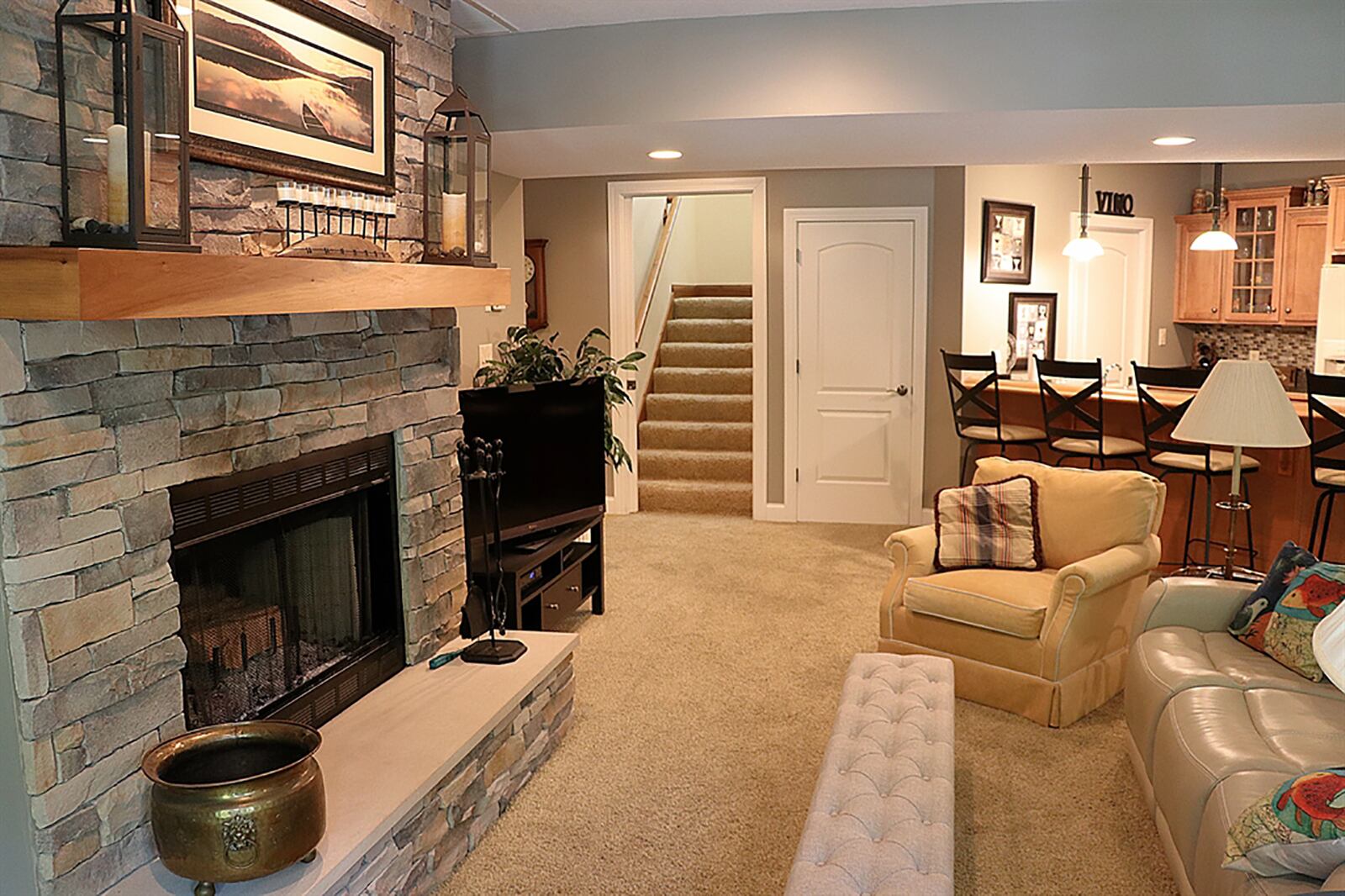 At the bottom of the open stairwell, a pocket door opens into the lower-level family room with a gas fireplace and wet bar area. The stack-stone fireplace has a wood-beam mantel and raised hearth. CONTRIBUTED PHOTO BY KATHY TYLER