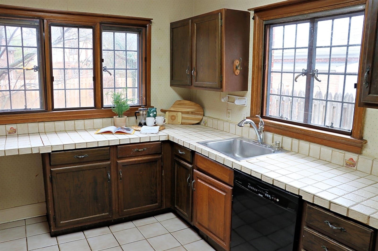 Ceramic-tile counters complement the dark cabinetry that fills three walls of the kitchen. The sink is below a window, and triple windows fill a preparation area with natural light. 