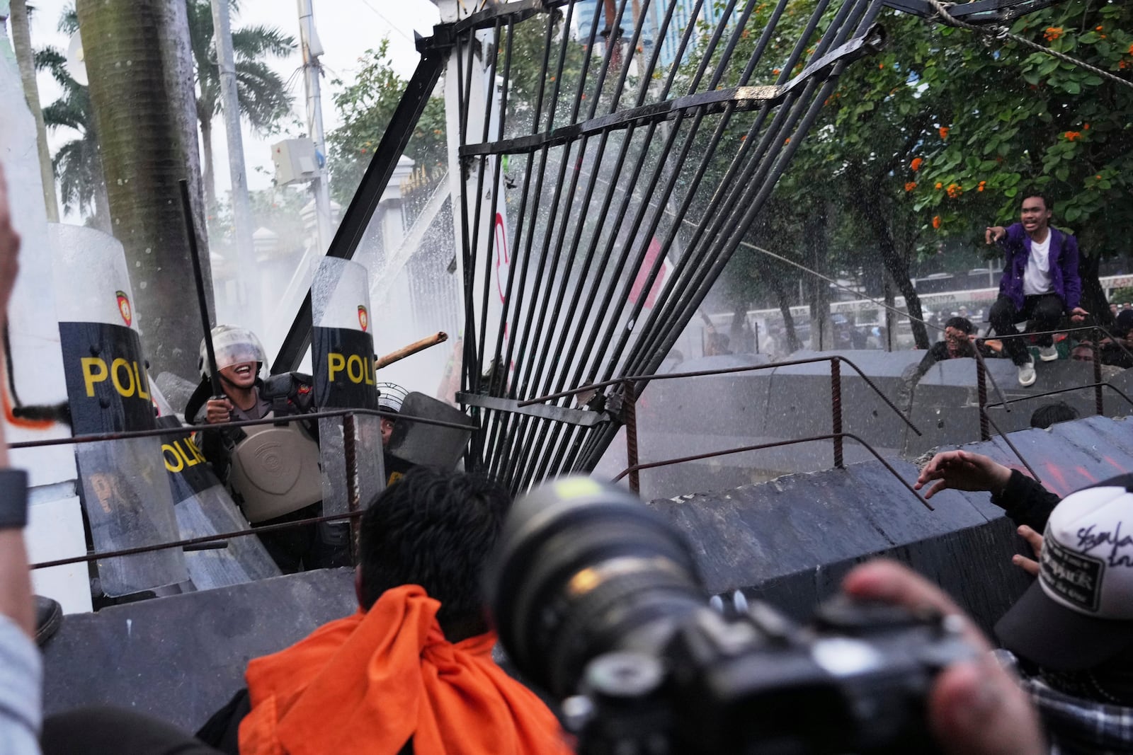 Riot police officers react as protesters tear down part of the fence of the parliament building during a rally in Jakarta, Indonesia, Thursday, March 20, 2025, against the passing of a controversial revision of a military law that will allow military officers to serve in more government posts without resigning from the armed forces. (AP Photo/Tatan Syuflana)