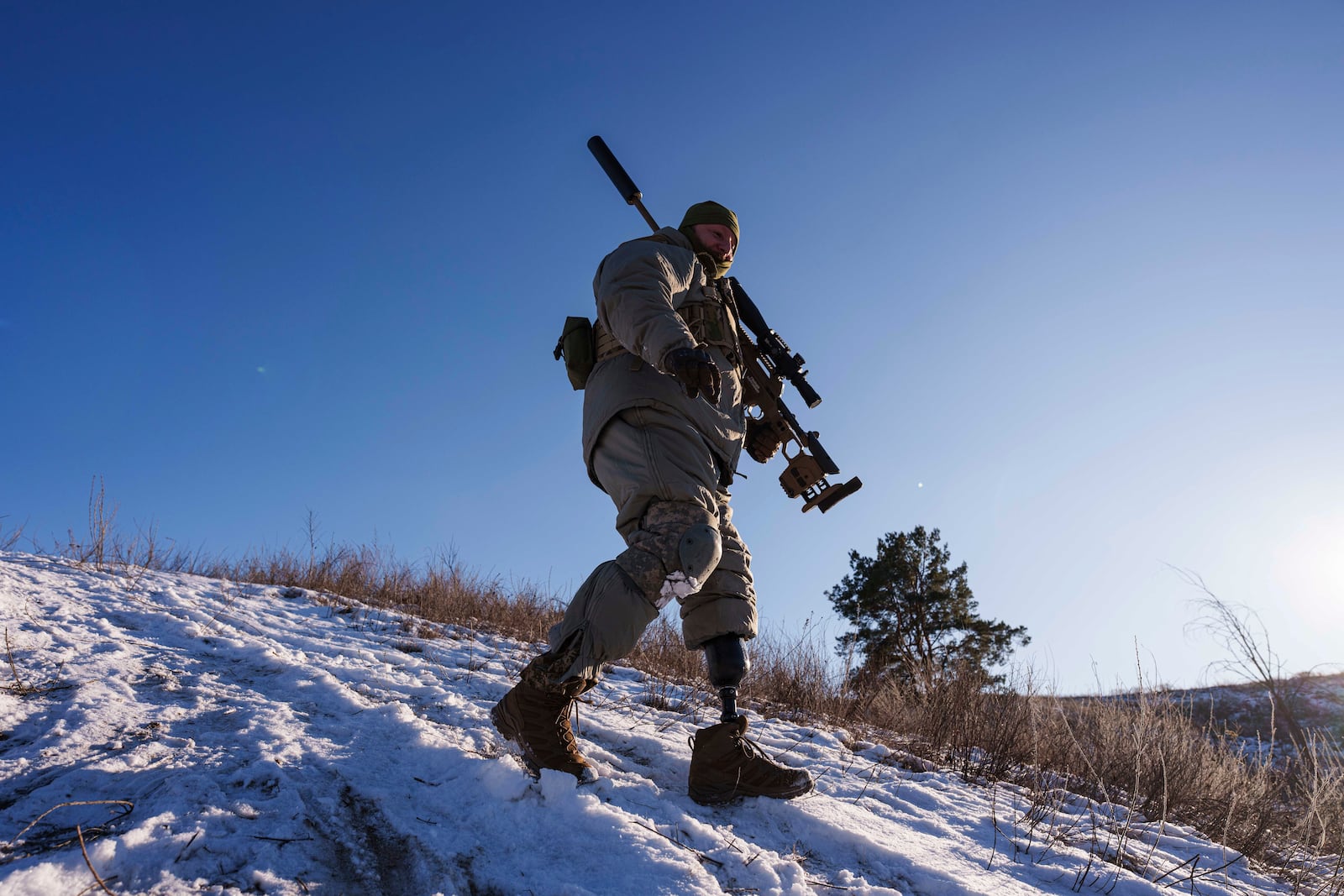 Serhii Pozniak, a commander with a Ukrainian sniper unit who lost a leg after stepping on a mine, carries his rifle during training near Kyiv, Ukraine on Feb. 17, 2025. (AP Photo/Evgeniy Maloletka)