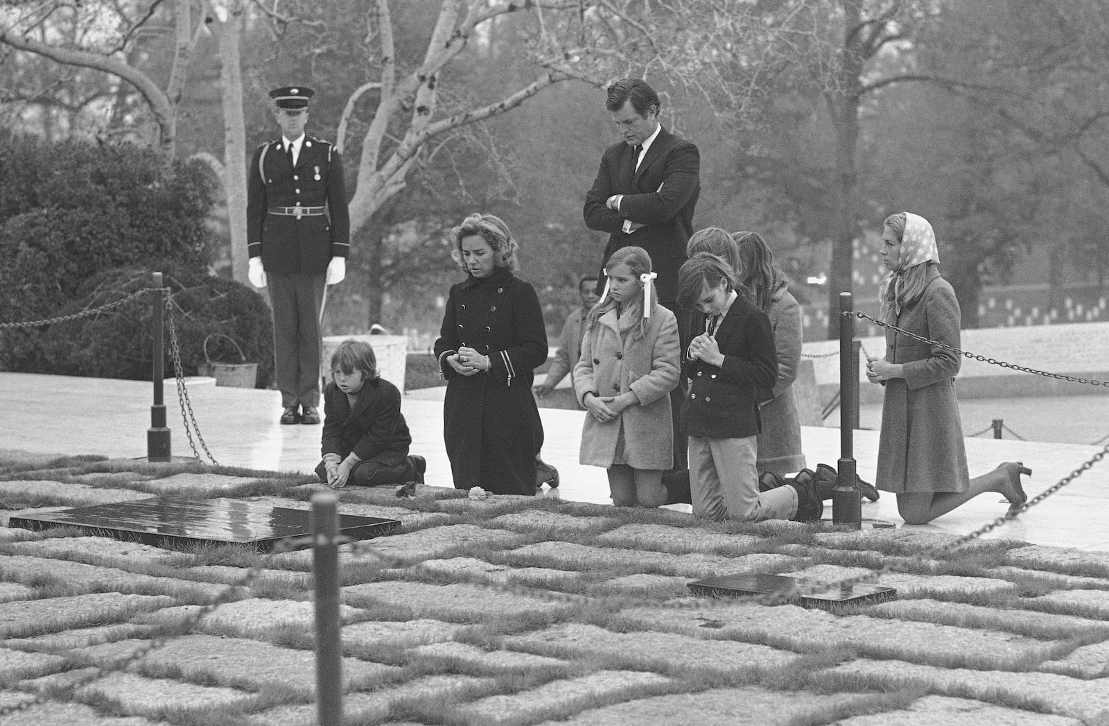 FILE - Sen. Edward Kennedy, back, stands behind the widow of former Senator Robert F. Kennedy, Mrs. Ethel Kennedy, second left, with her five children, and his wife Joan, right, as they pause at the grave of assassinated President John F. Kennedy in Arlington National Cemetery, Nov. 20, 1970, in Arlington, Va. (AP Photo/Bob Daugherty, File)