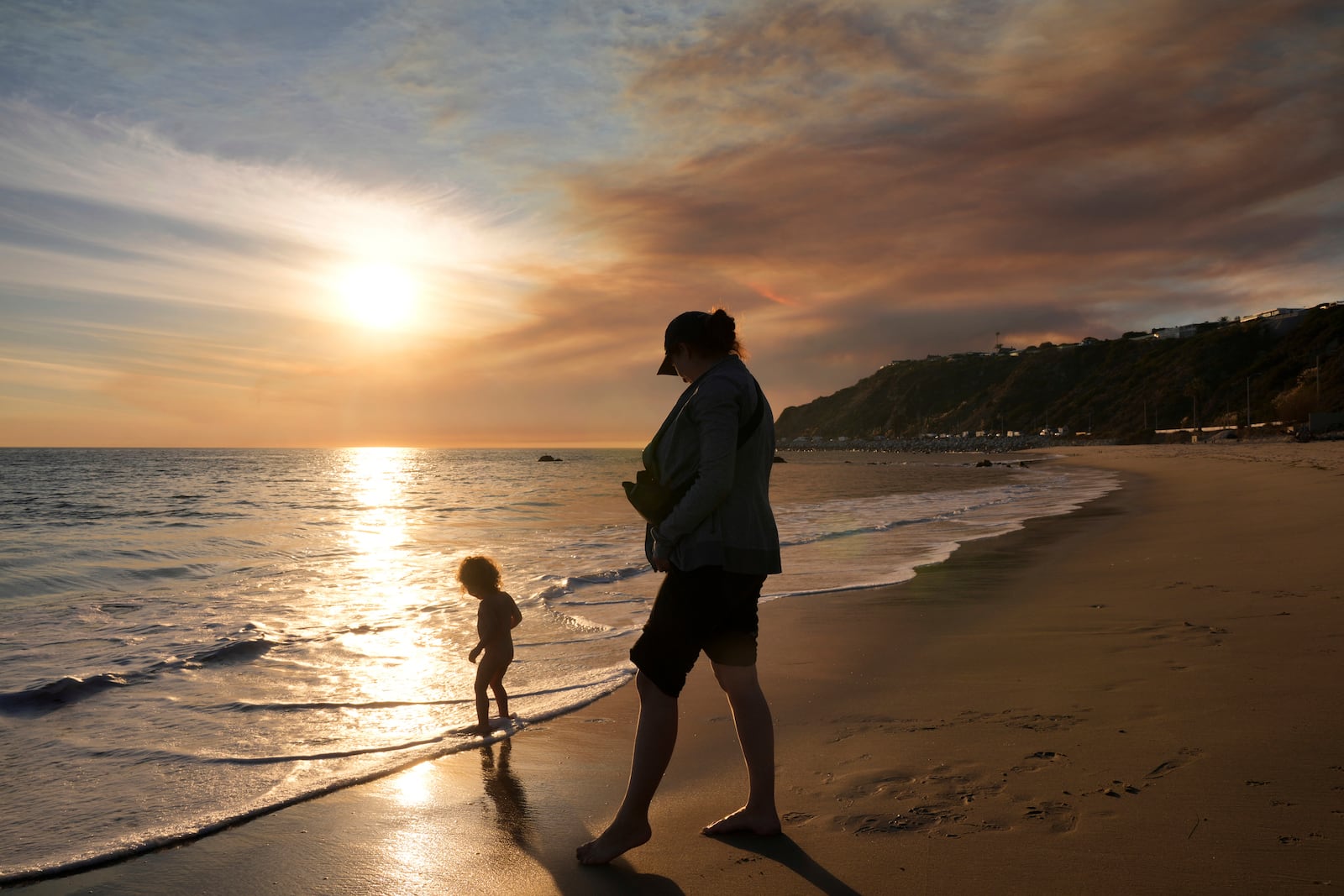 Malibu residents Florence Johnson and her son Brian enjoy the beach before sunset as a plume of smoke from the Franklin Fire rises over the ocean Tuesday, Dec. 10, 2024, in Malibu, Calif. (AP Photo/Damian Dovarganes)