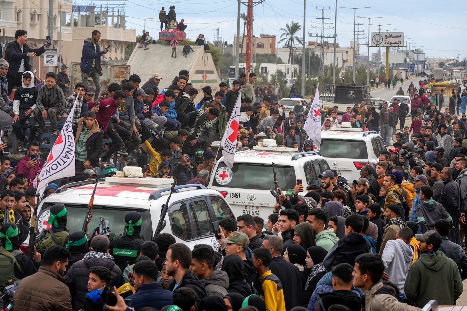 Palestinians gather as Hamas fighters escort Red Cross vehicles carrying Israeli captives Ohad Ben Ami, Eli Sharabi, and Or Levy, who have been held hostage by Hamas in Gaza since October 7, 2023, after being handed over in Deir al-Balah, central Gaza Strip, Saturday, Feb. 8, 2025. (AP Photo/Abdel Kareem Hana)