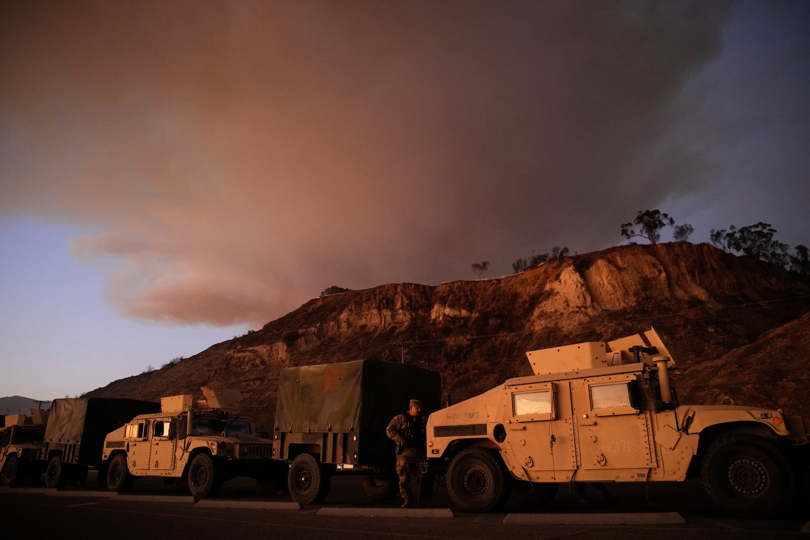 California National Guard line up along the Pacific Coast Highway as a plume of smoke rises from the Palisades Fire on Friday, Jan. 10, 2025, in the Pacific Palisades section of Los Angeles. (AP Photo/John Locher)