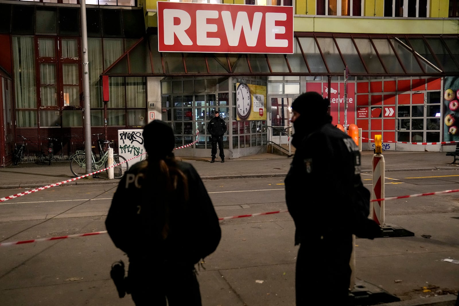 Police officers stand guard in front of a Rewe Market after a knife attack, in Berlin, Germany, Tuesday, Dec. 31, 2024. (AP Photo/Ebrahim Noroozi)