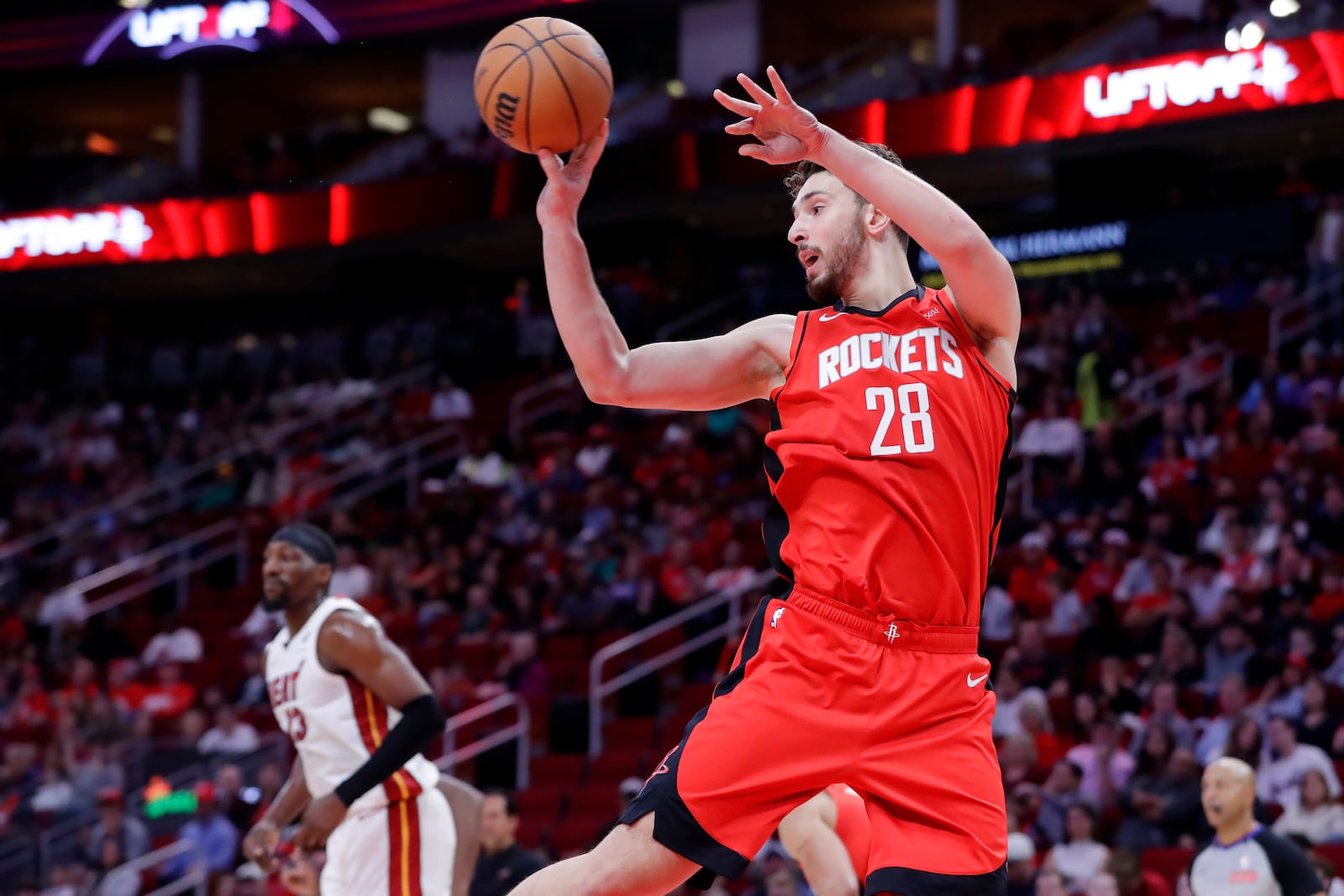 Houston Rockets center Alperen Sengun (28) dishes off a rebound as Miami Heat center Bam Adebayo, left, looks on during the first half of an NBA basketball game, Sunday, Dec. 29, 2024, in Houston. (AP Photo/Michael Wyke)