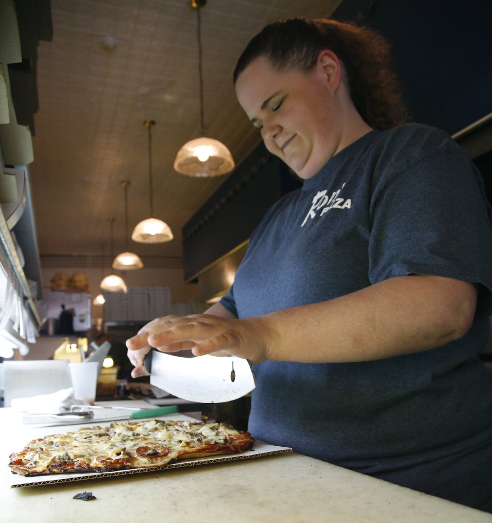 Ron Holp, the proprietor of Ron’s Pizza and Ribs, has been making pizza for 42 years. He started Dayton’s first “Pizza War” when he left Cassano’s to start his own pizza place On St. Patrick’s Day, 1964, he and his late wife Abbie opened Ron’s Pizza on North 12th Street in Miamisburg. Ron’s Pizza employee Emily Young cuts a fresh pizza for a lunch customer.