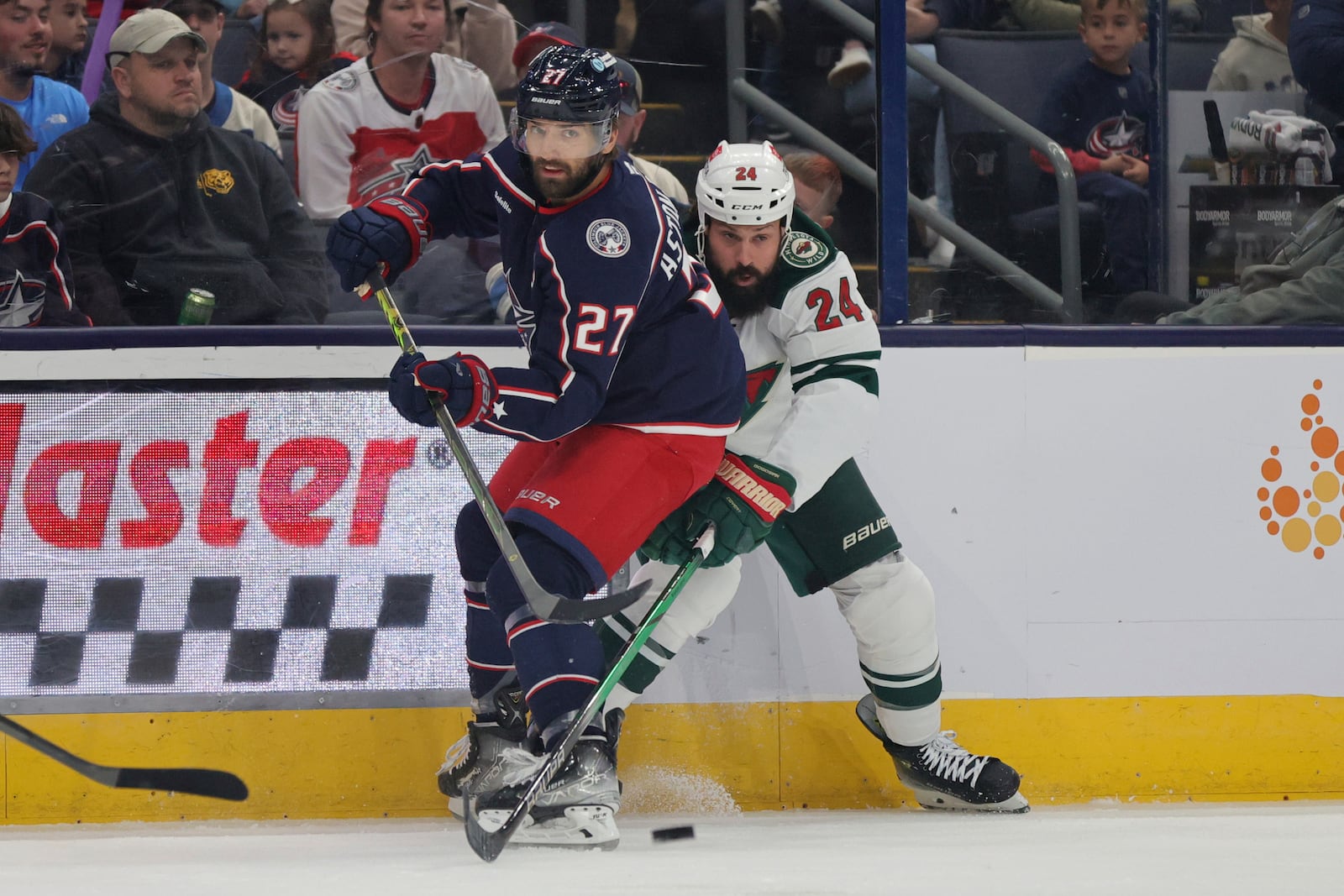 Columbus Blue Jackets forward Mathieu Olivier, left, passes the puck in front of Minnesota Wild defenseman Zach Bogosian during the first period of an NHL hockey game in Columbus, Ohio, Saturday, Oct. 19, 2024. (AP Photo/Paul Vernon)